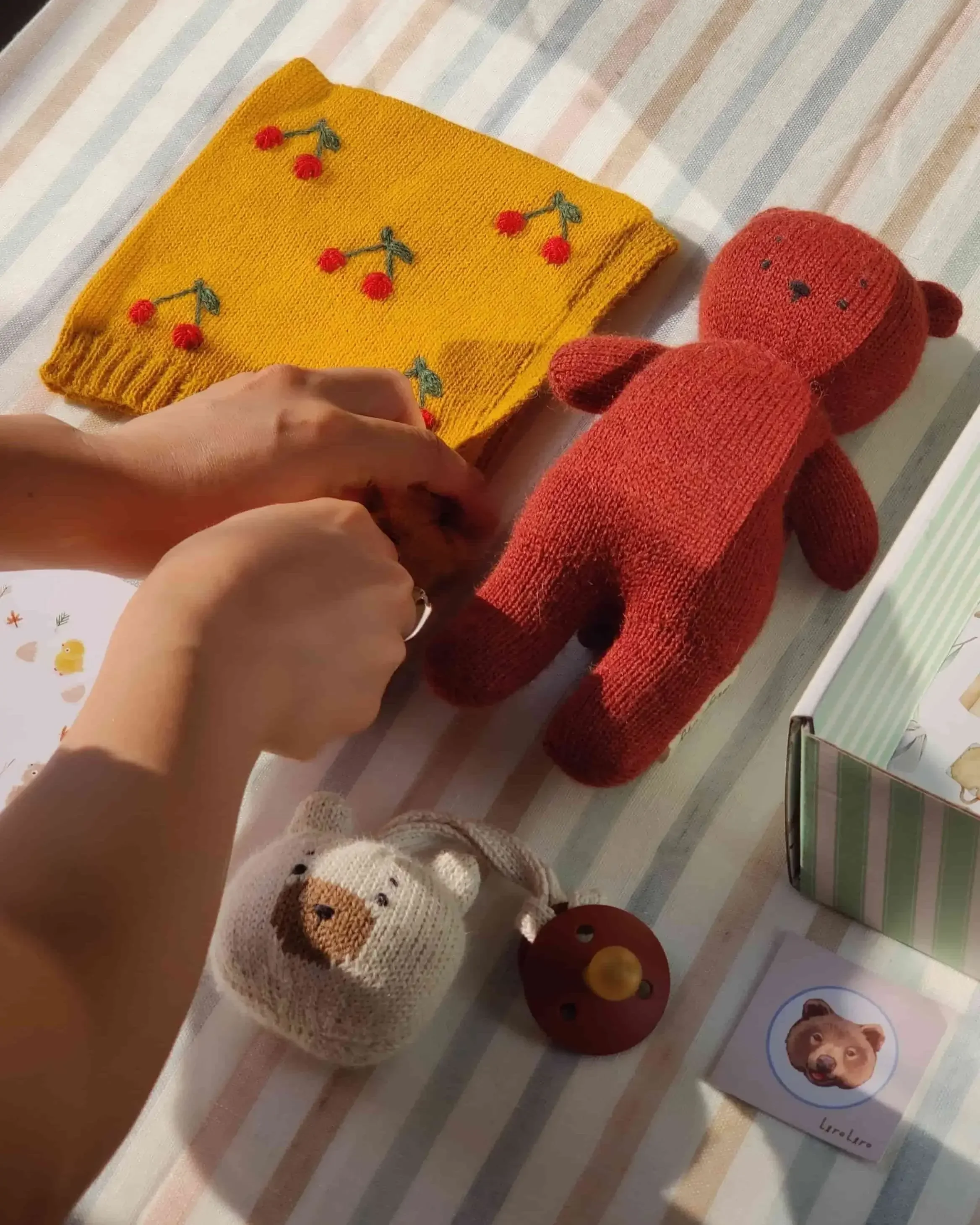 Composition du coffret naissance Alpaga rouge cerise : un ourson Teddy Bear en alpaga terracotta, un mini-Teddy attache-tétine en alpaga blanc et un bonnet béguin jaune avec broderies de cerises