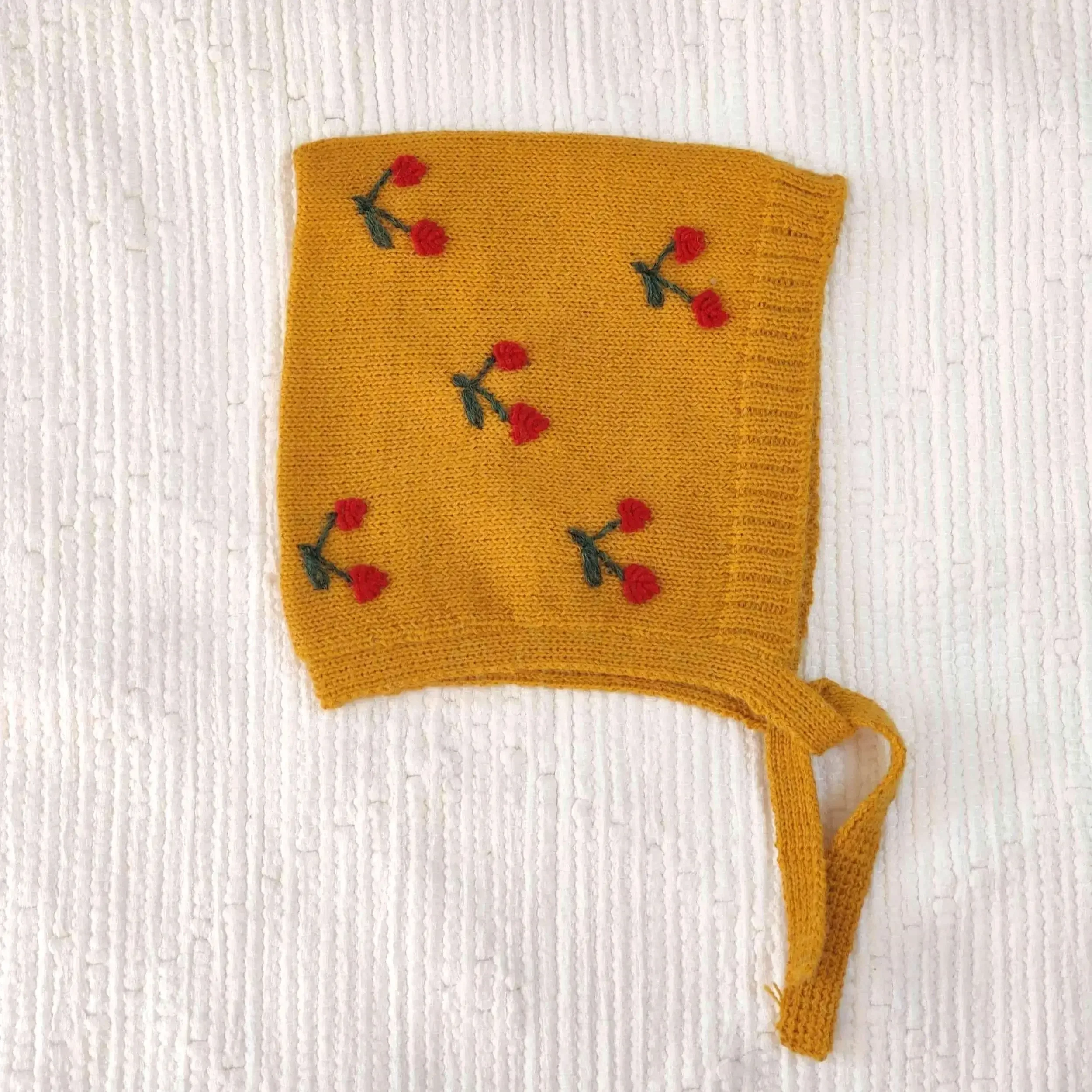 Le bonnet béguin pour bébé en alpaga jaune avec des broderies artisanales de cerises