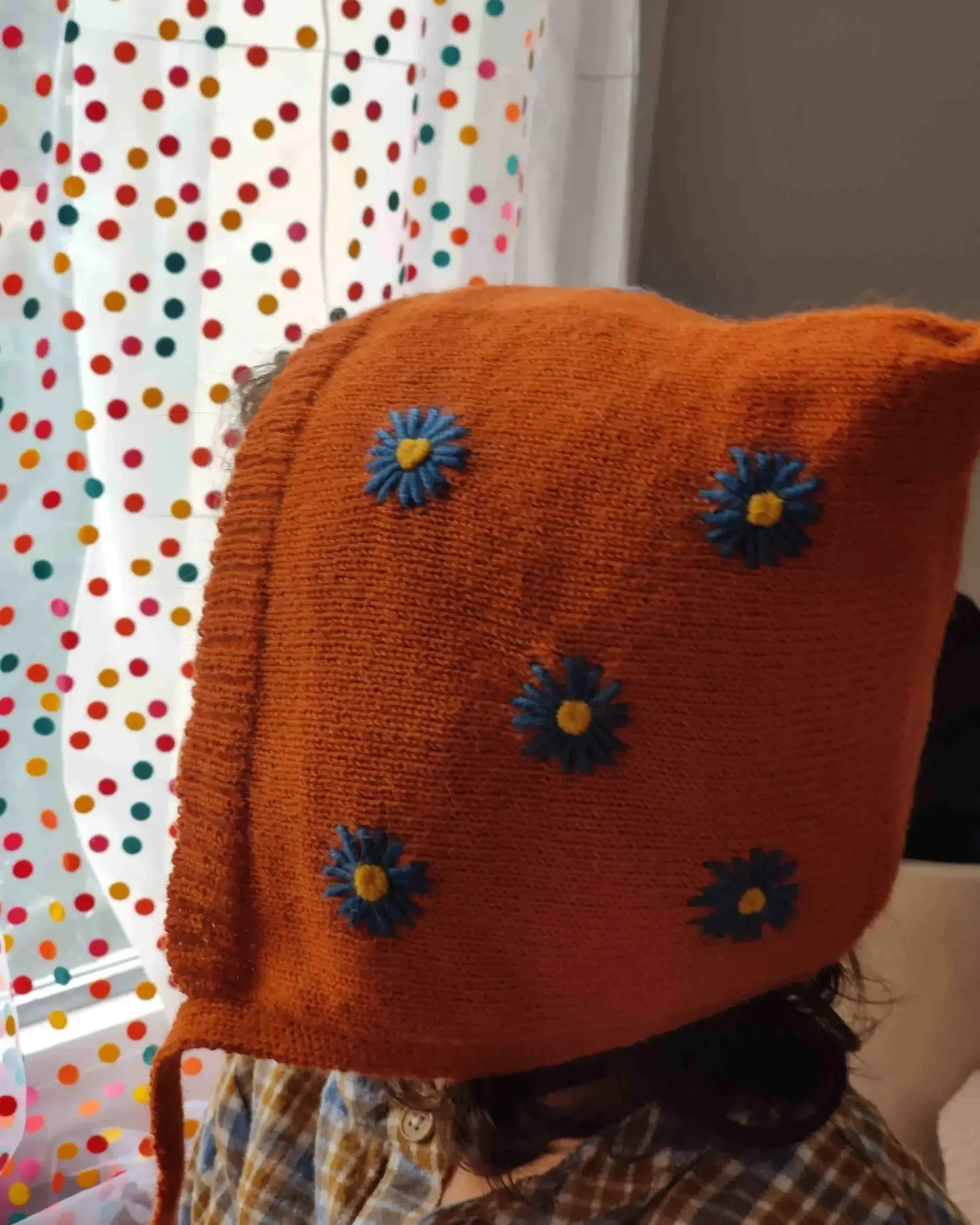 Bébé portant un bonnet béguin en alpaga terracotta avec des broderies de bleuet