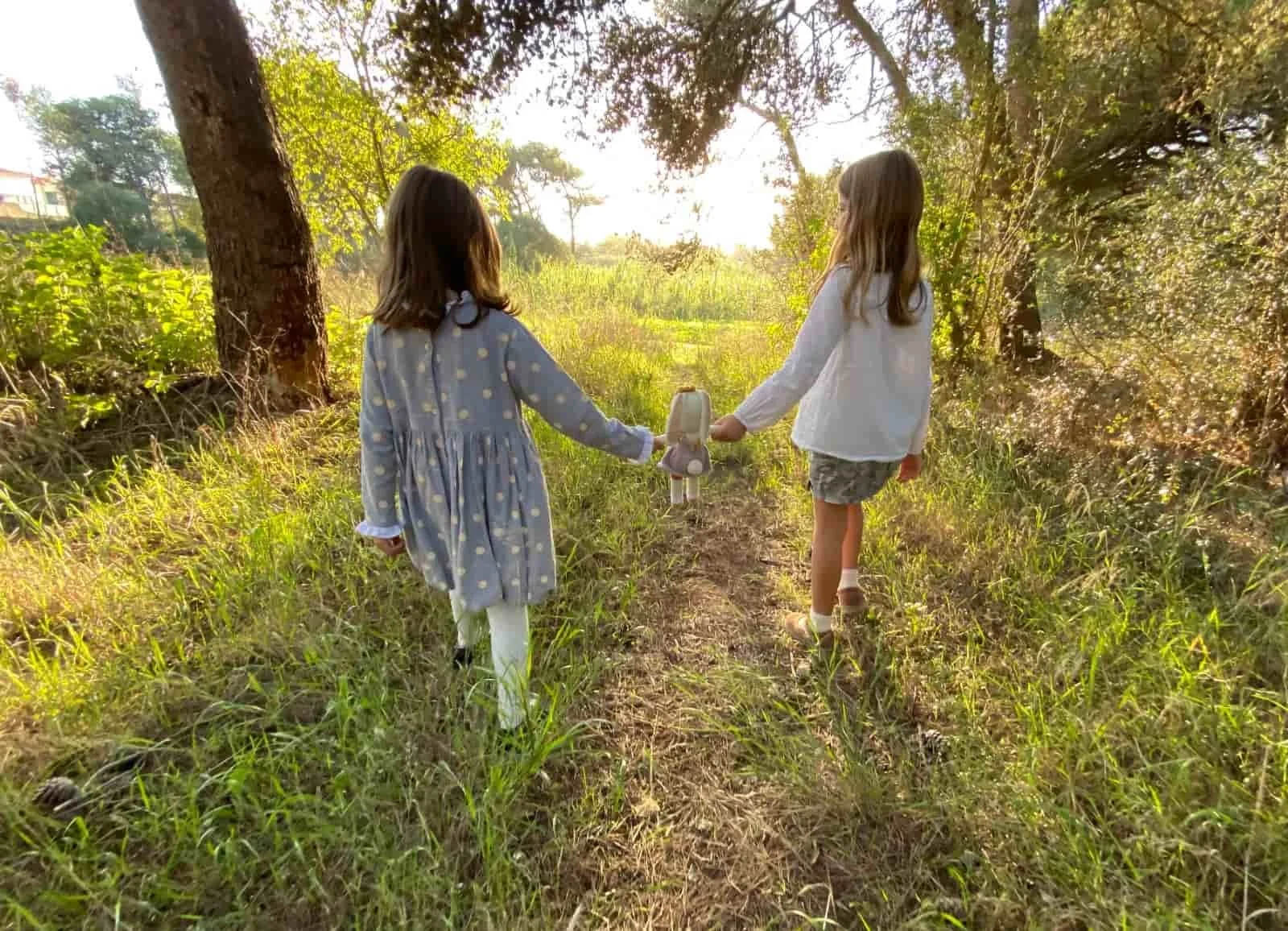 Deux jeunes filles marchent dans la forêt en tenant par la main une peluche des émotions en coton bio