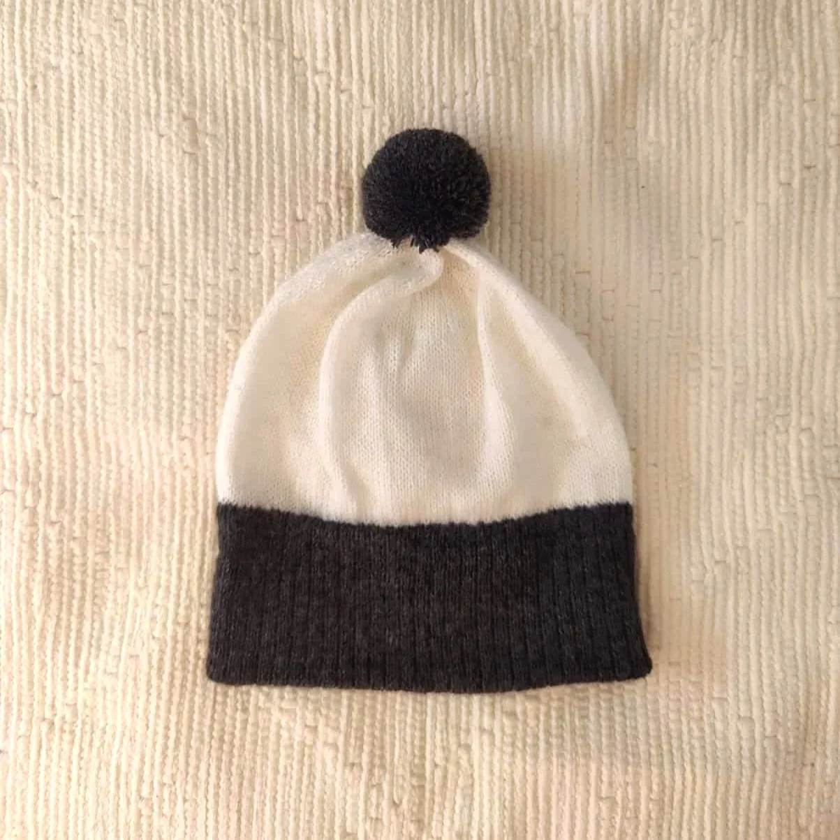 Bonnet artisanal tricoté en laine blanc avec pompon et revers noirs pour enfant