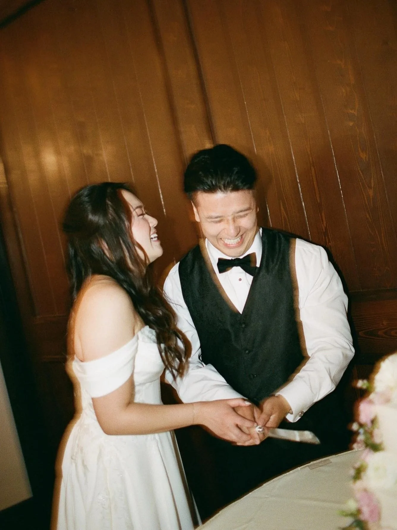 A bride and groom smiling and holding hands during their wedding ceremony in front of a wooden wall.