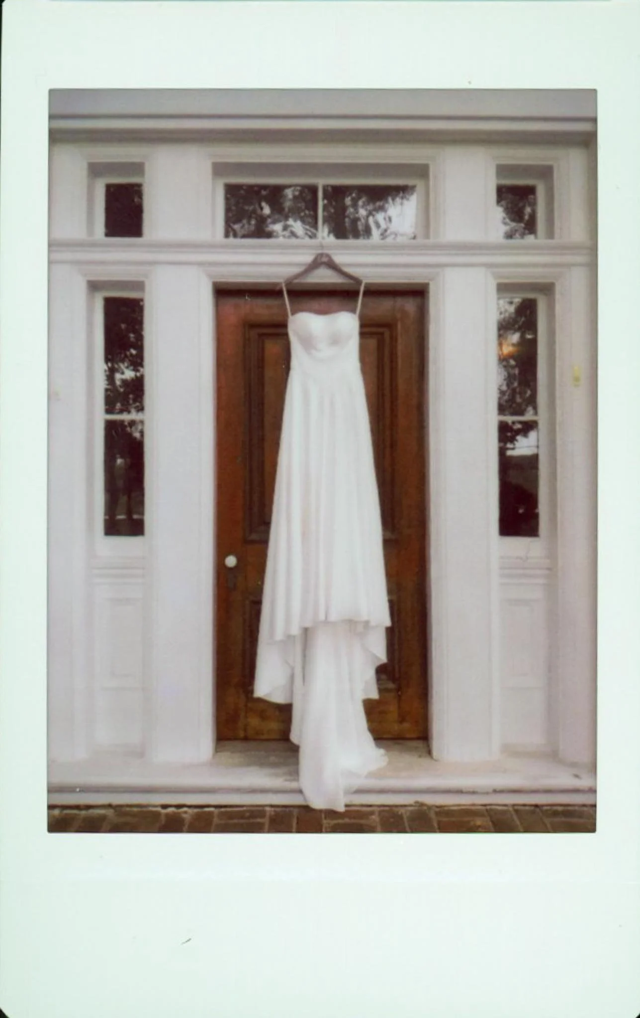 A white wedding dress hanging on a hanger on a door, with glass panels on either side.