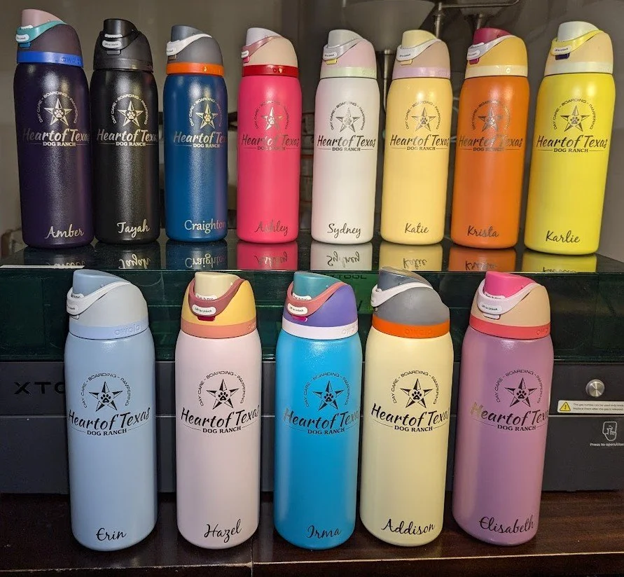 Colorful personalized water bottles with 'Heart of Texas Dog Ranch' logo and individual names, arranged on shelves.