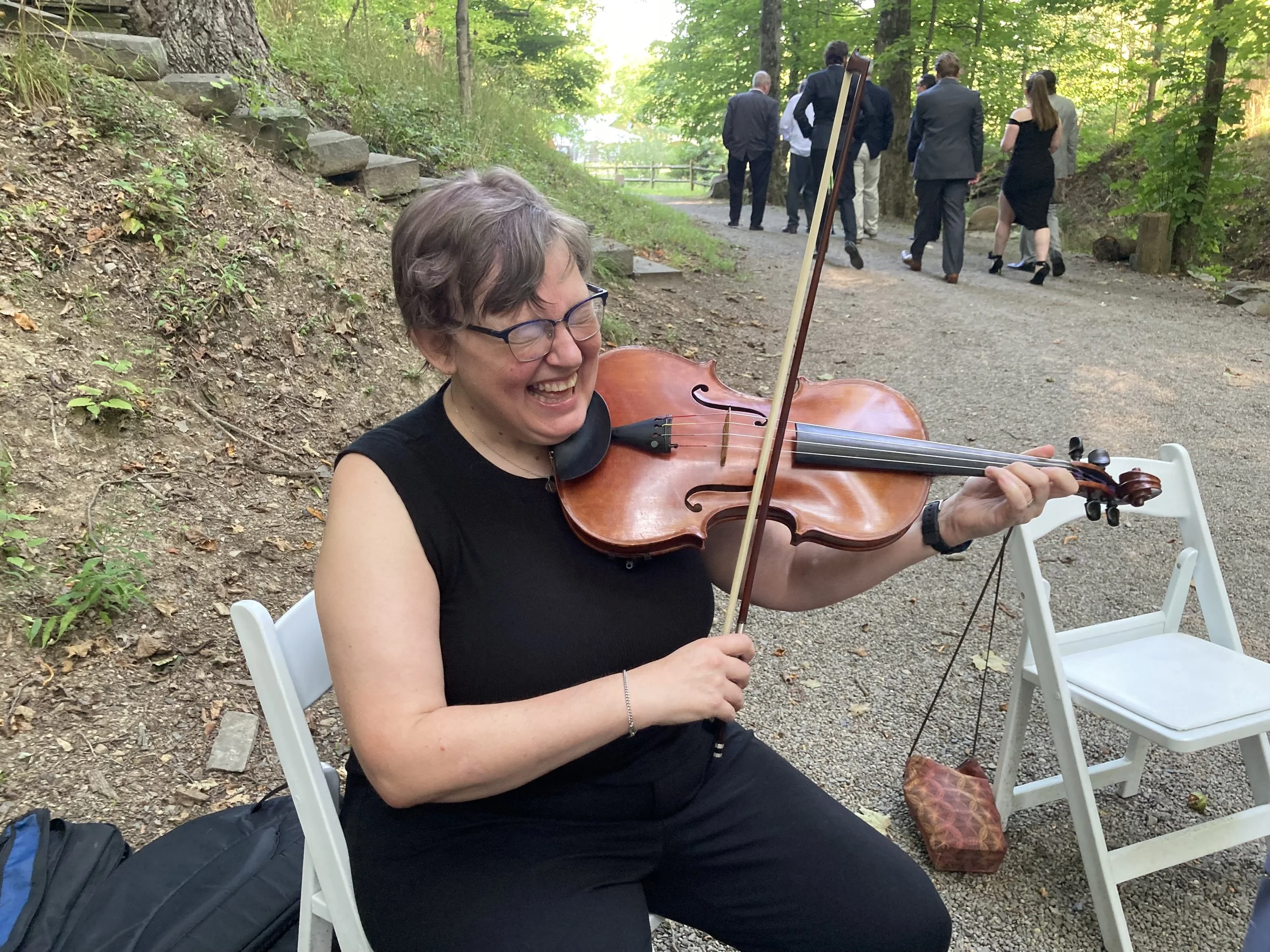 Aara laughs while playing her viola outdoors in the woods.