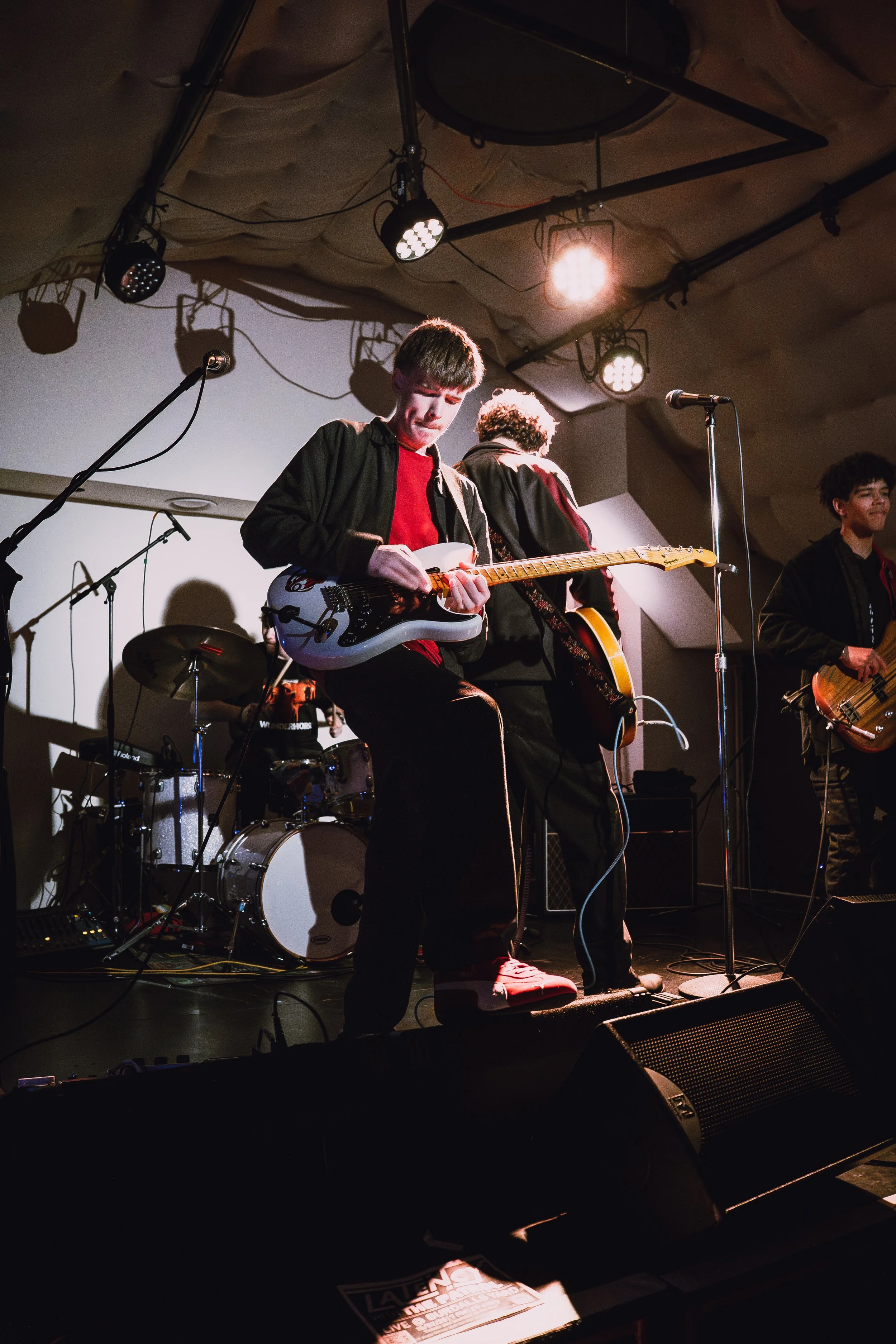 A band performing live on stage, with several members playing guitars and drums, under warm stage lighting.