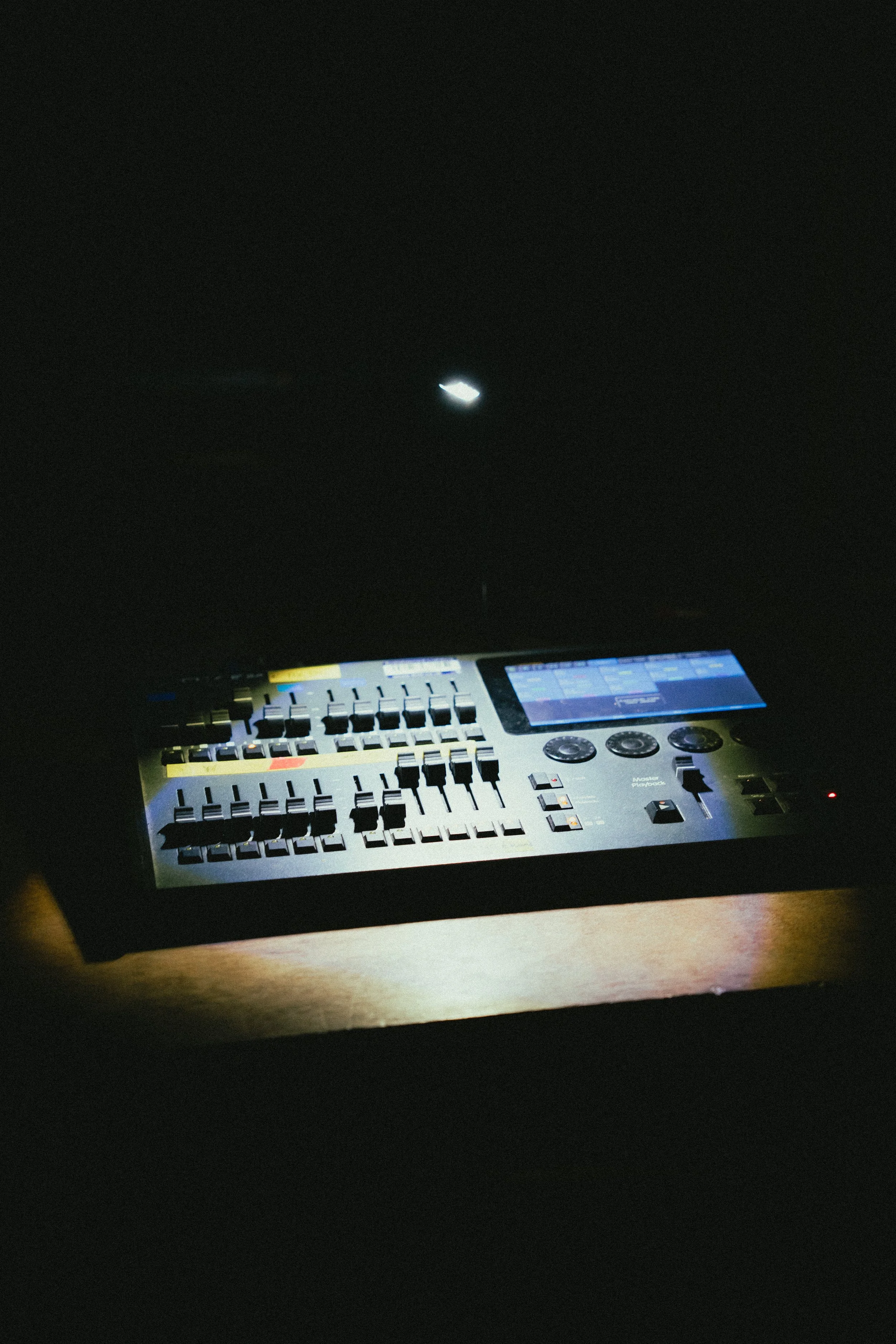 A music production device with various sliders, buttons, and a touchscreen, placed on a wooden surface in a dark environment.