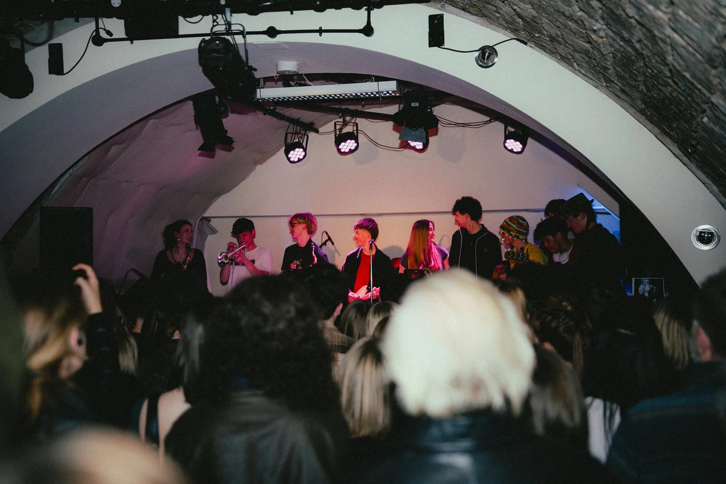 Group of young musicians performing on stage in a cozy venue, audience watching.