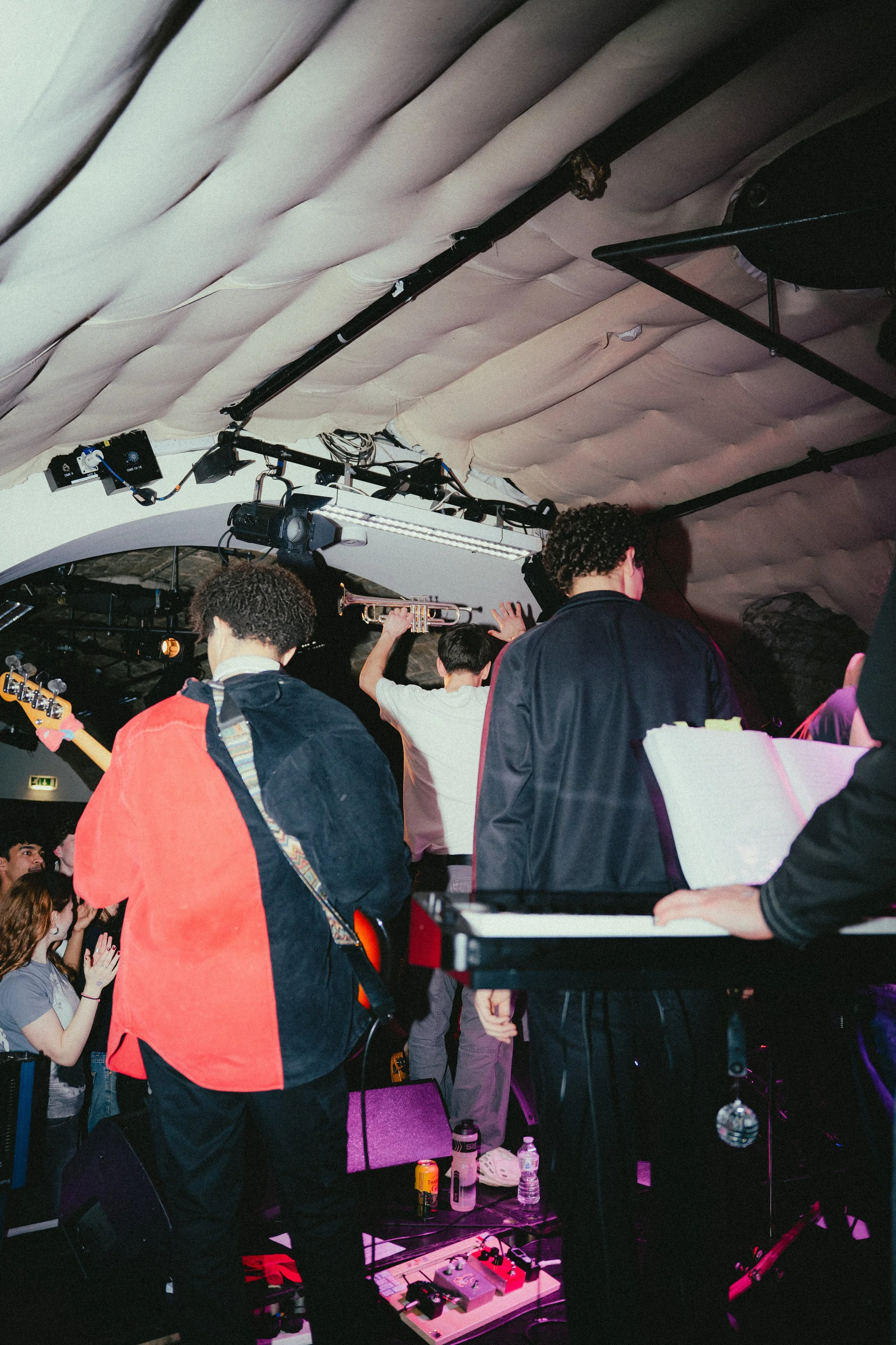 People on a stage with musical instruments in a venue, with one person holding a trumpet and others preparing to perform.
