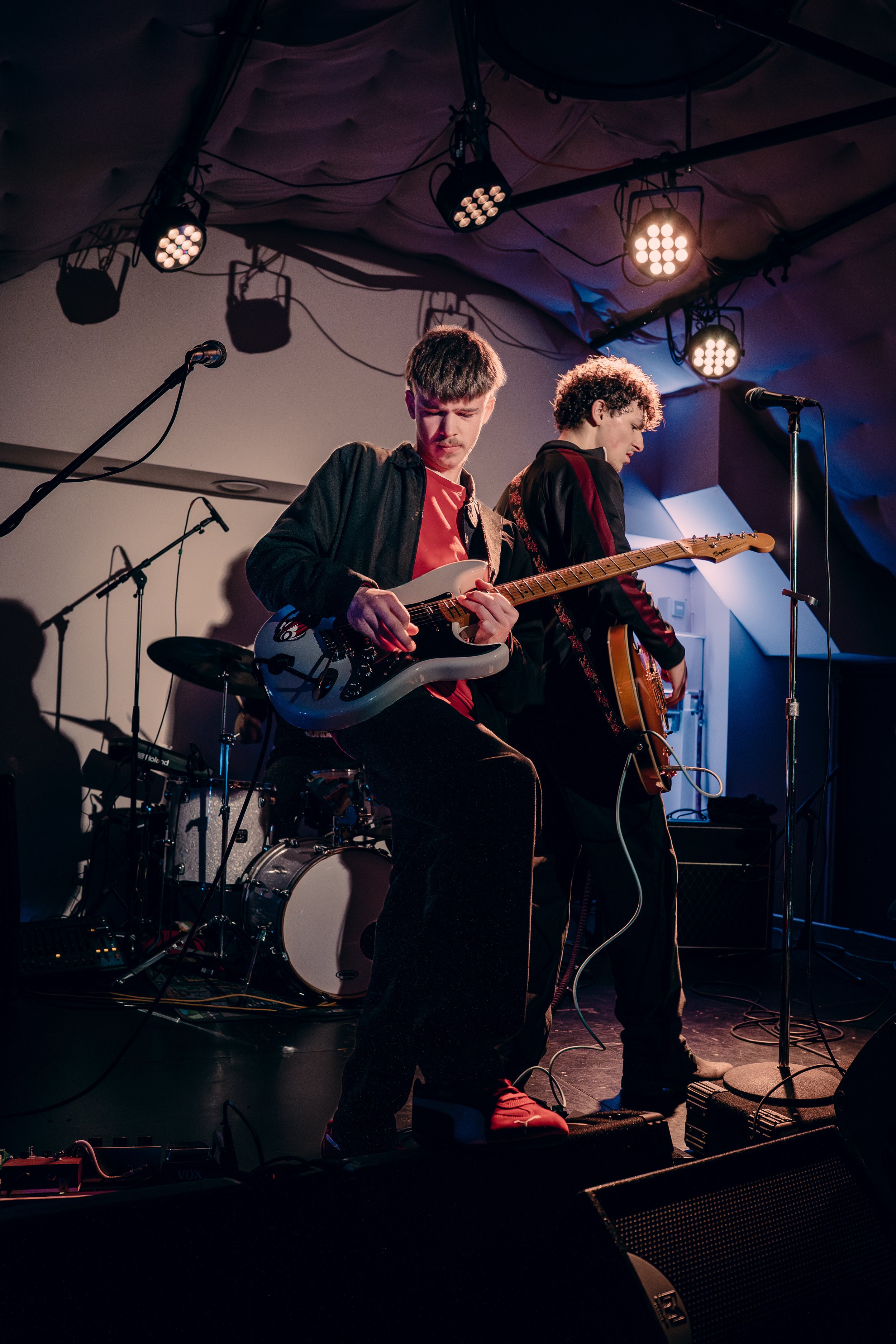 Two young men playing electric guitars on stage during a live music performance.