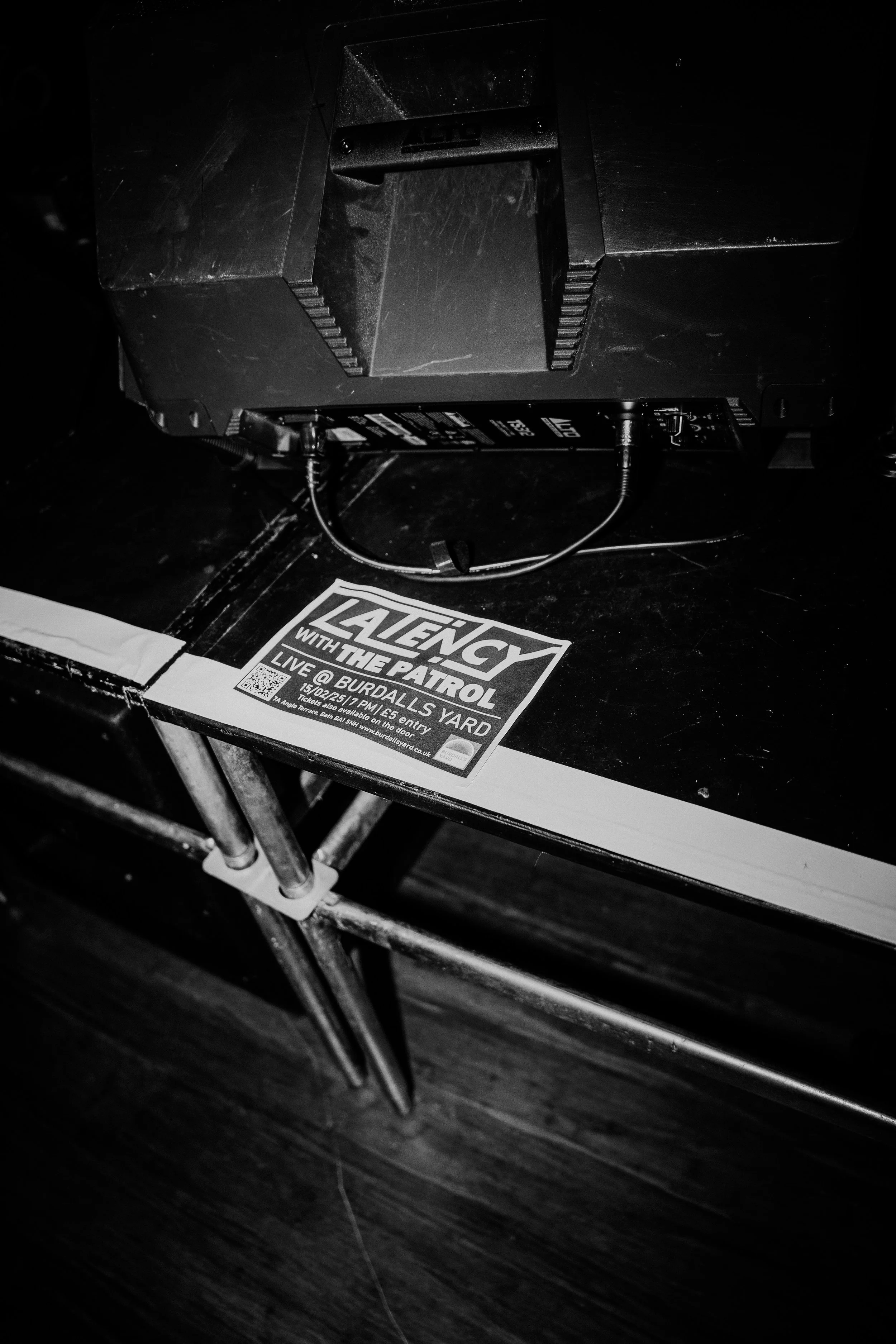 Black and white photo showing a table with a promotional flyer for an event at Burdalls Yard and a large electronic device with cables on top.