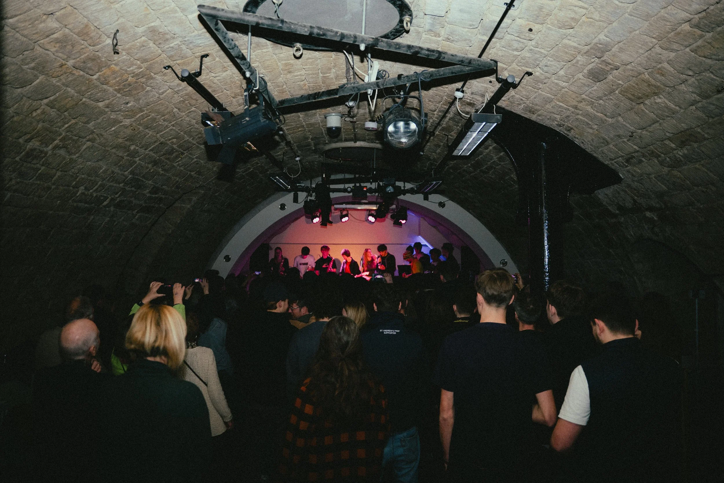 Crowd attending a live musical performance in an underground venue with exposed brick ceiling.