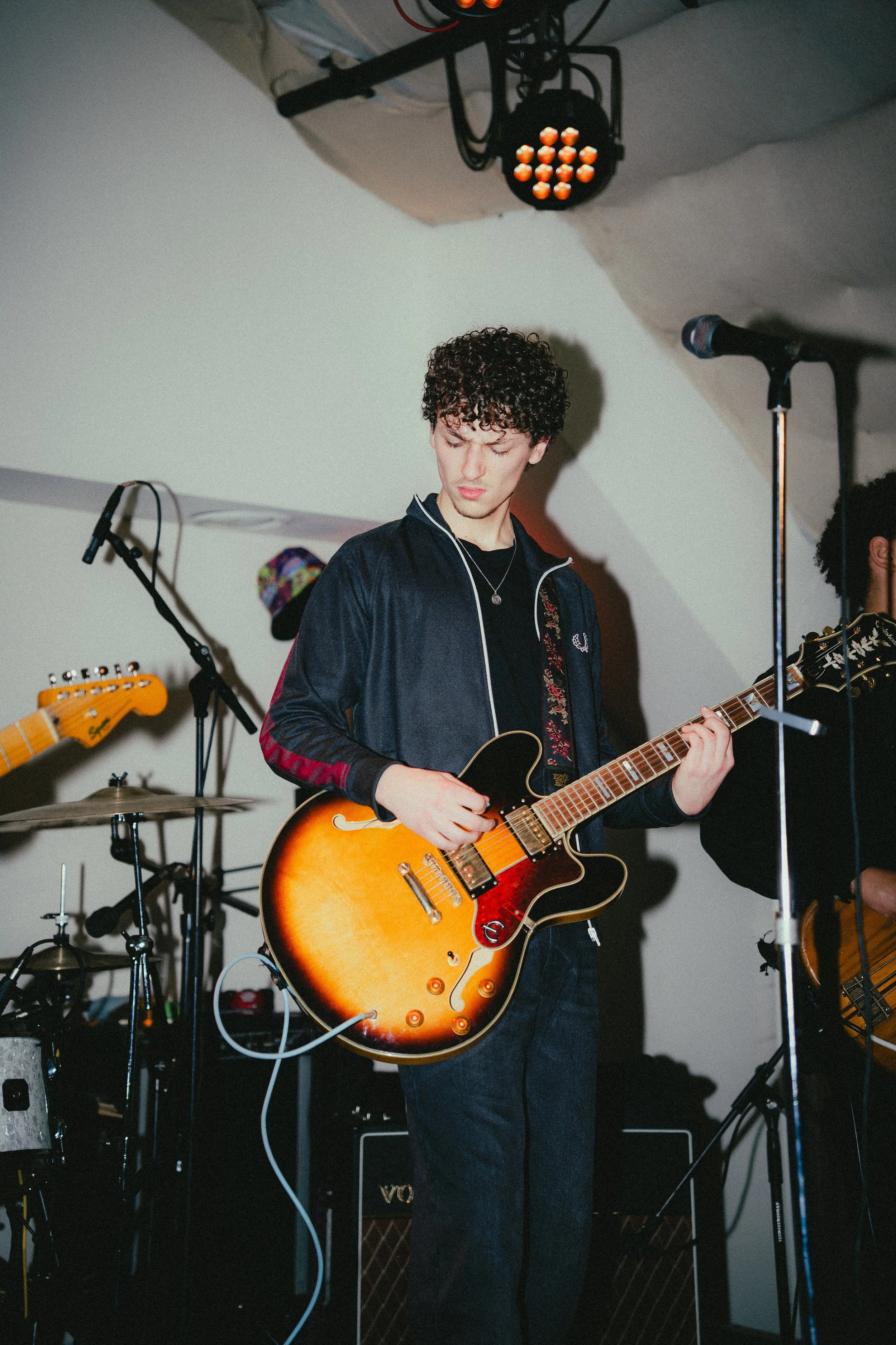 Young man with curly hair playing an electric guitar on stage during a music performance.