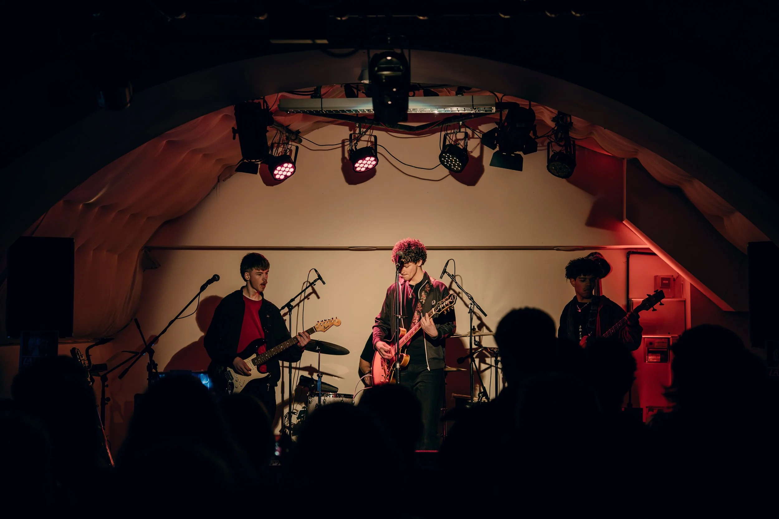 A band performing live on stage with three members playing guitars and singing into microphones, under stage lighting.