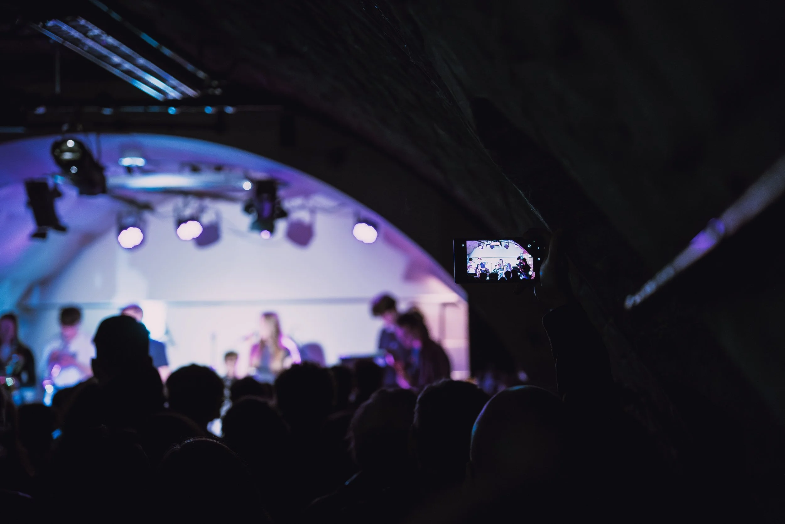 Person in the audience filming a concert or performance on their phone at an indoor venue.