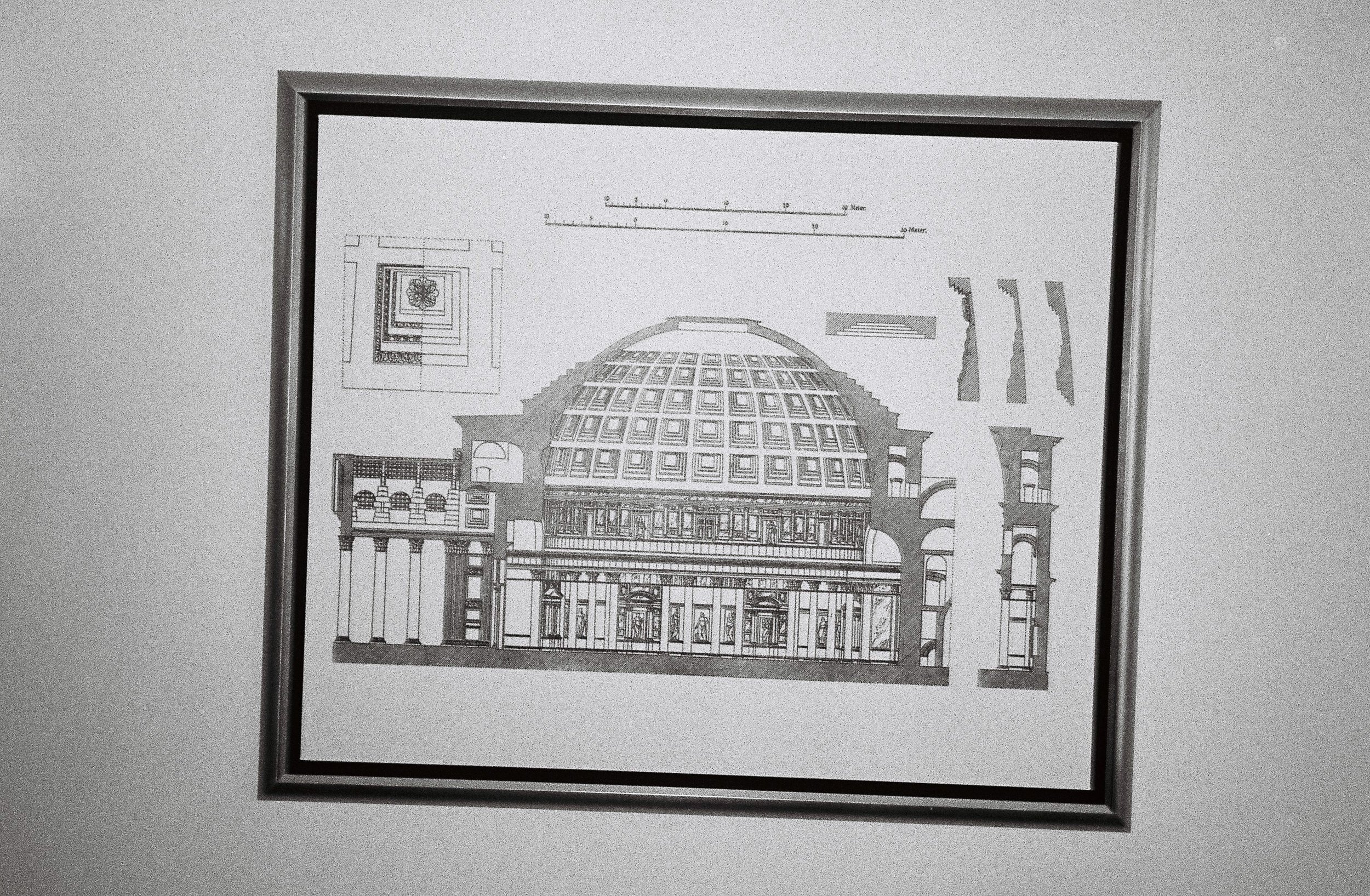 Architectural blueprint of a domed building with detailed interior and exterior sections, mounted on a wall.