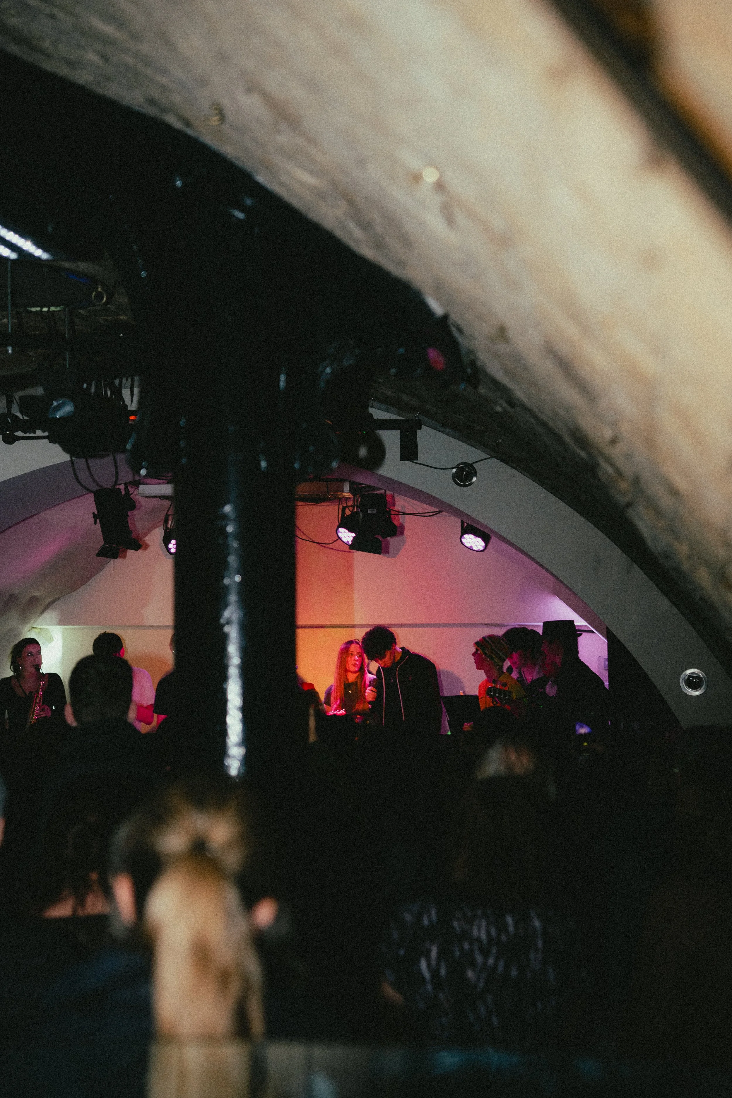 A live music concert with a band performing on stage, colorful lighting, and an audience watching.