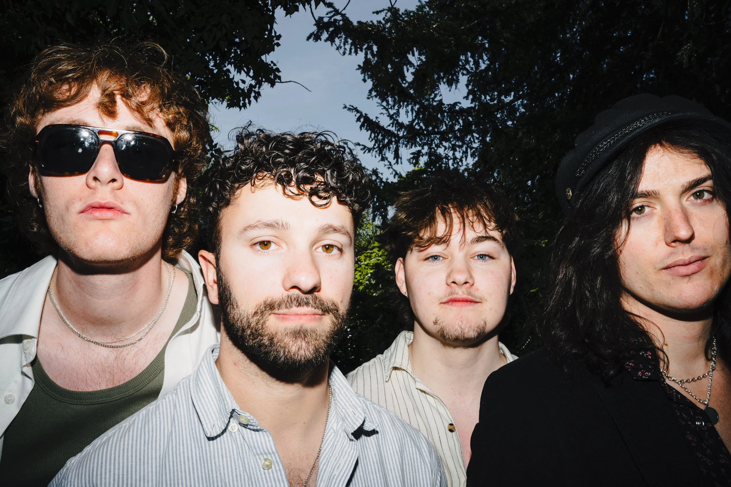 Close-up of five people standing outdoors, with a background of trees and a blue sky.