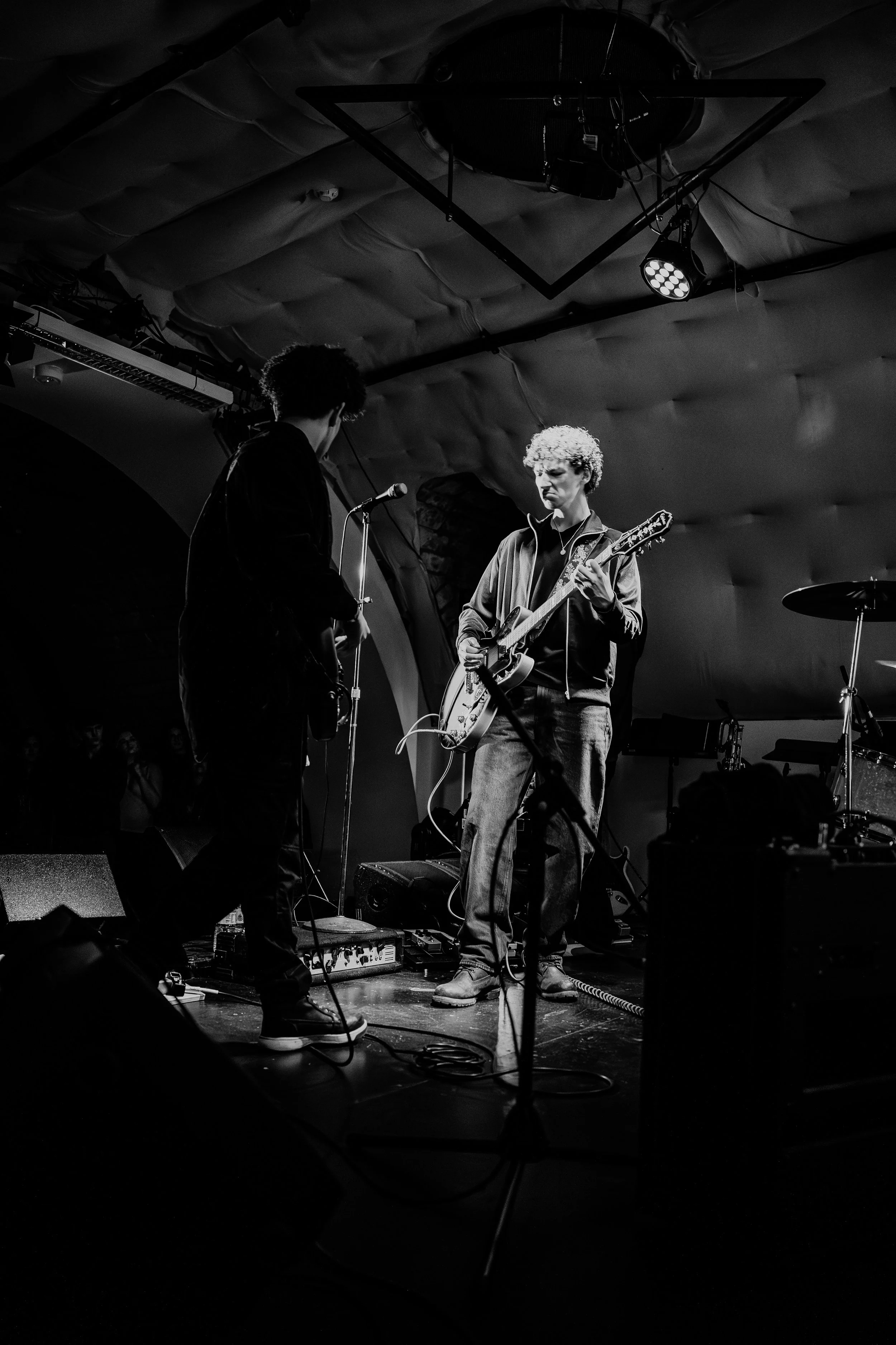 Two musicians playing guitars on stage during a live performance in a dark venue, black and white photo.