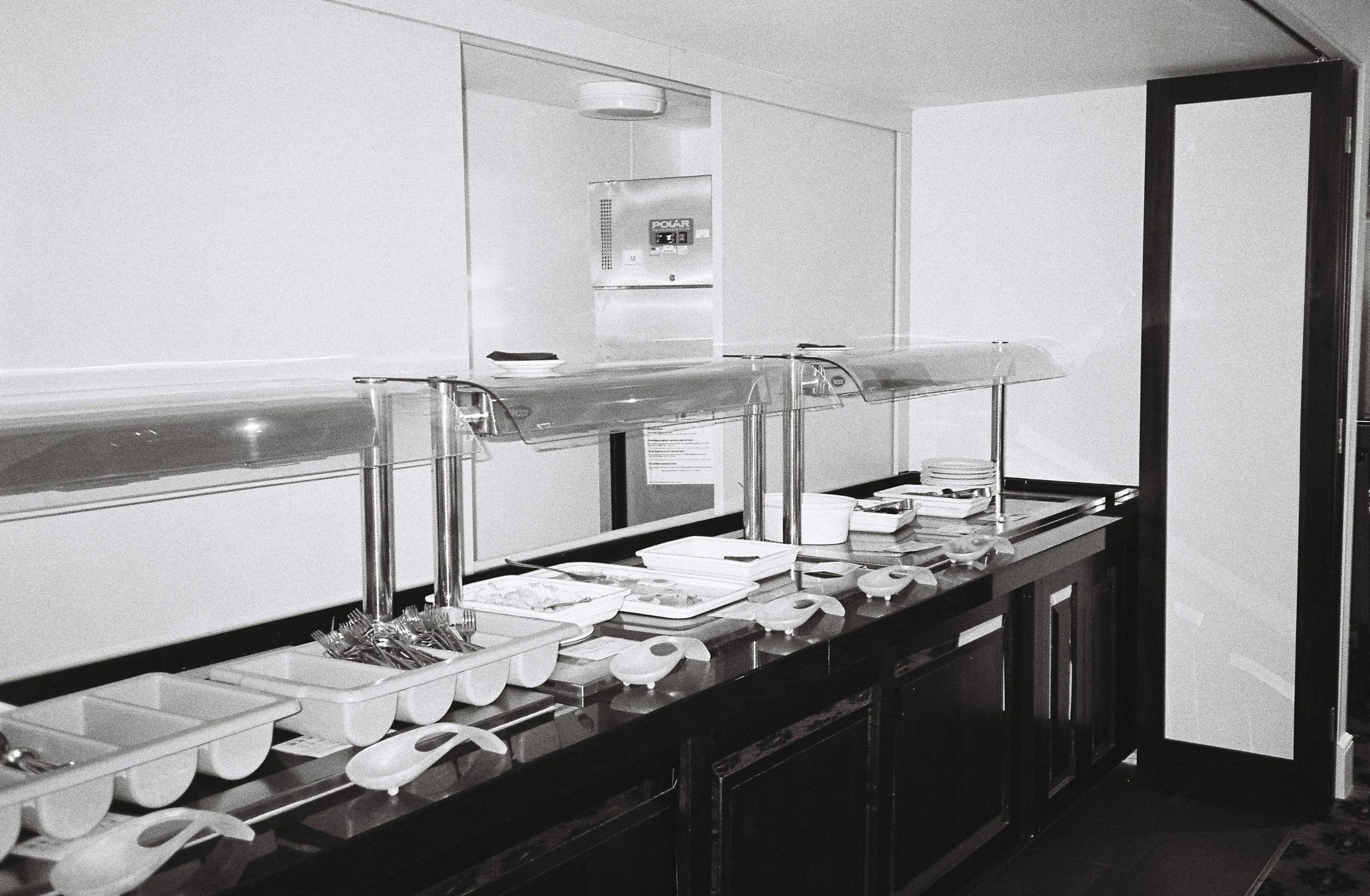 Buffet serving station with plates, utensils, and food trays in an indoor setting.