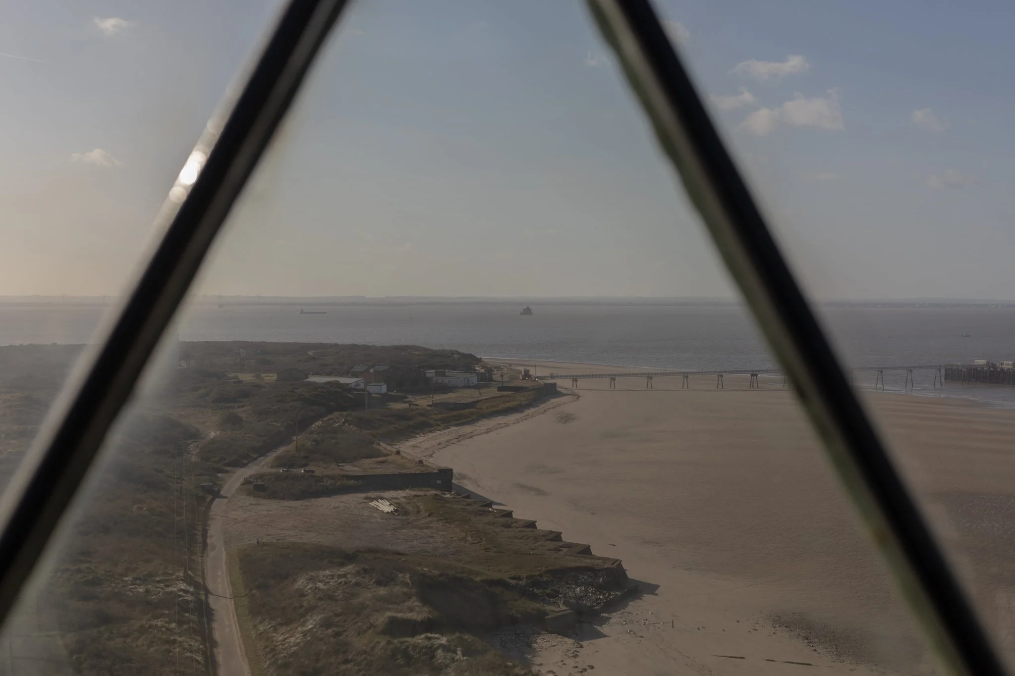 View of a beach and ocean seen from inside a lighthouse with the window frame visible.