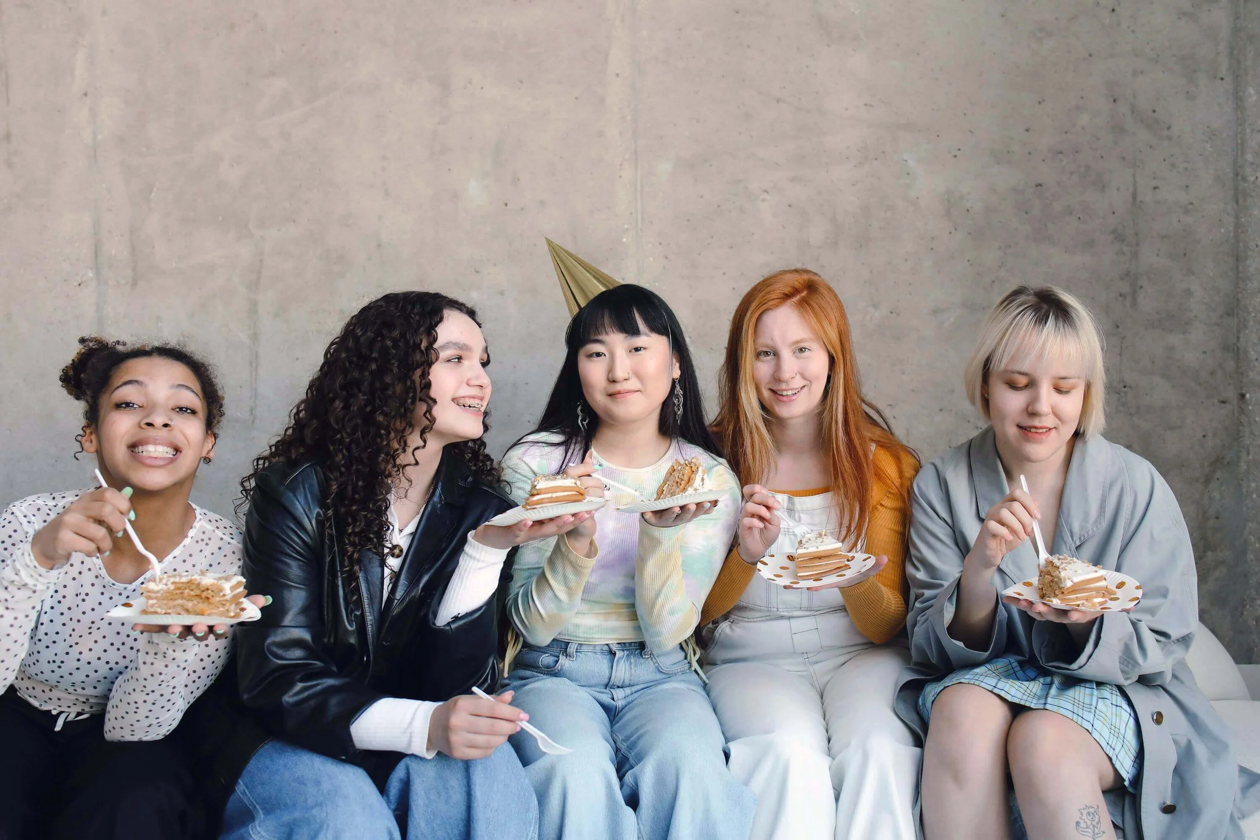 A group of girls with birthday hats on eating slices of cake
