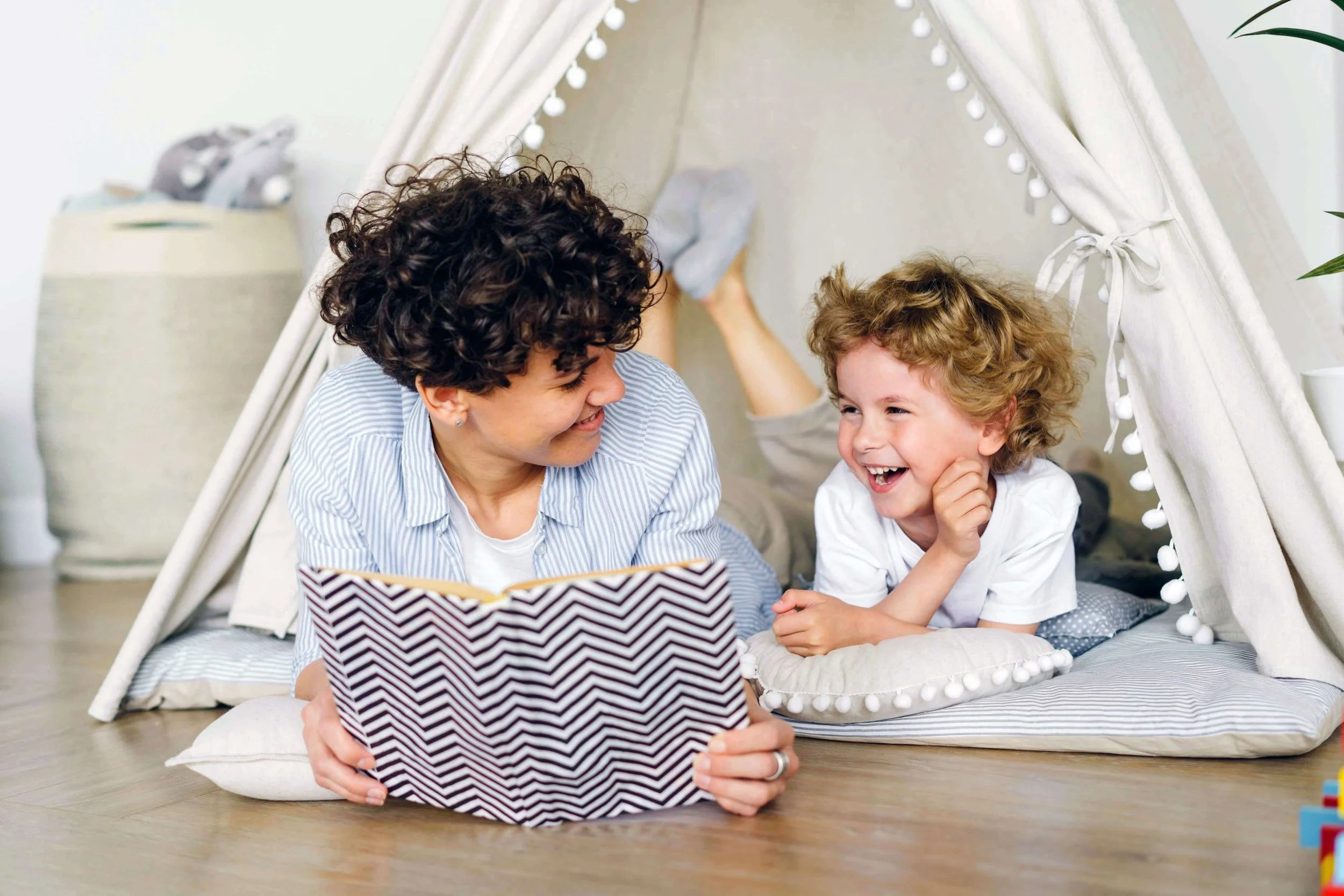 A parental figure and a child laying inside a canvas tent reading a book