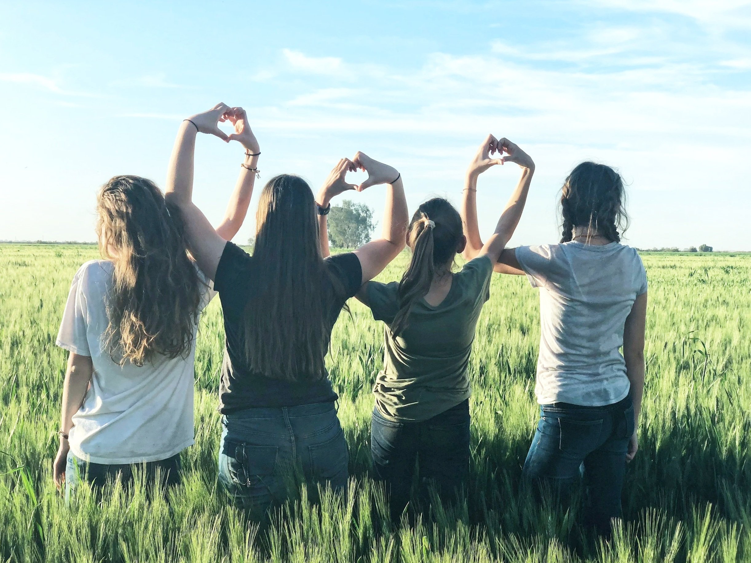 Four girls stand in a field. Their hands combine to form three hearts.
