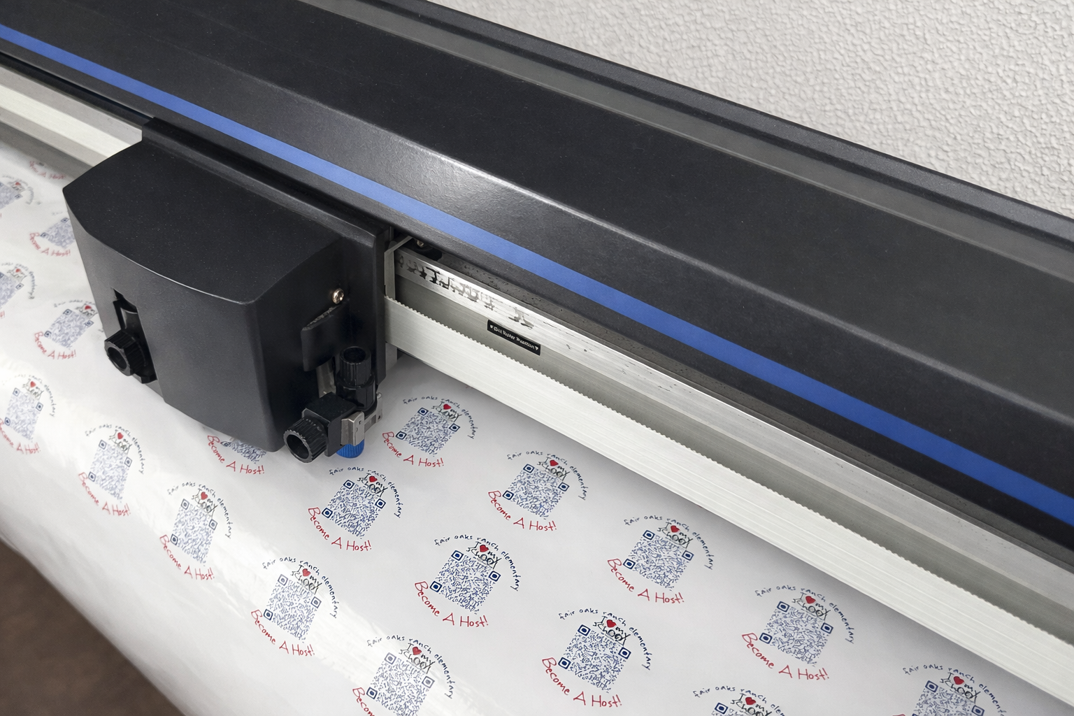 Digital cutting machine cutting paper printed with QR codes and the phrase 'Become A Host!'