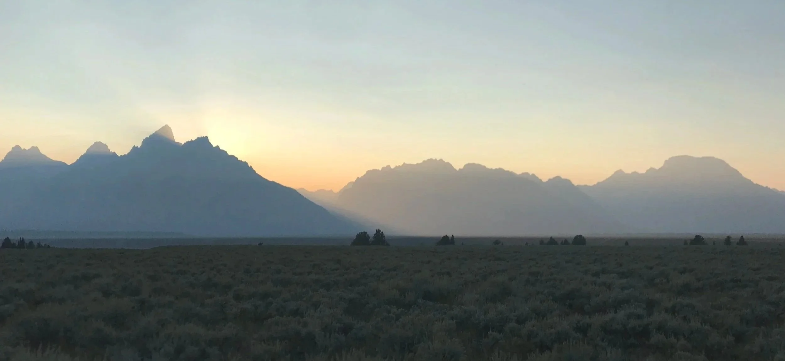 Sunset over a mountain range with a flat, grassy plain in the foreground.