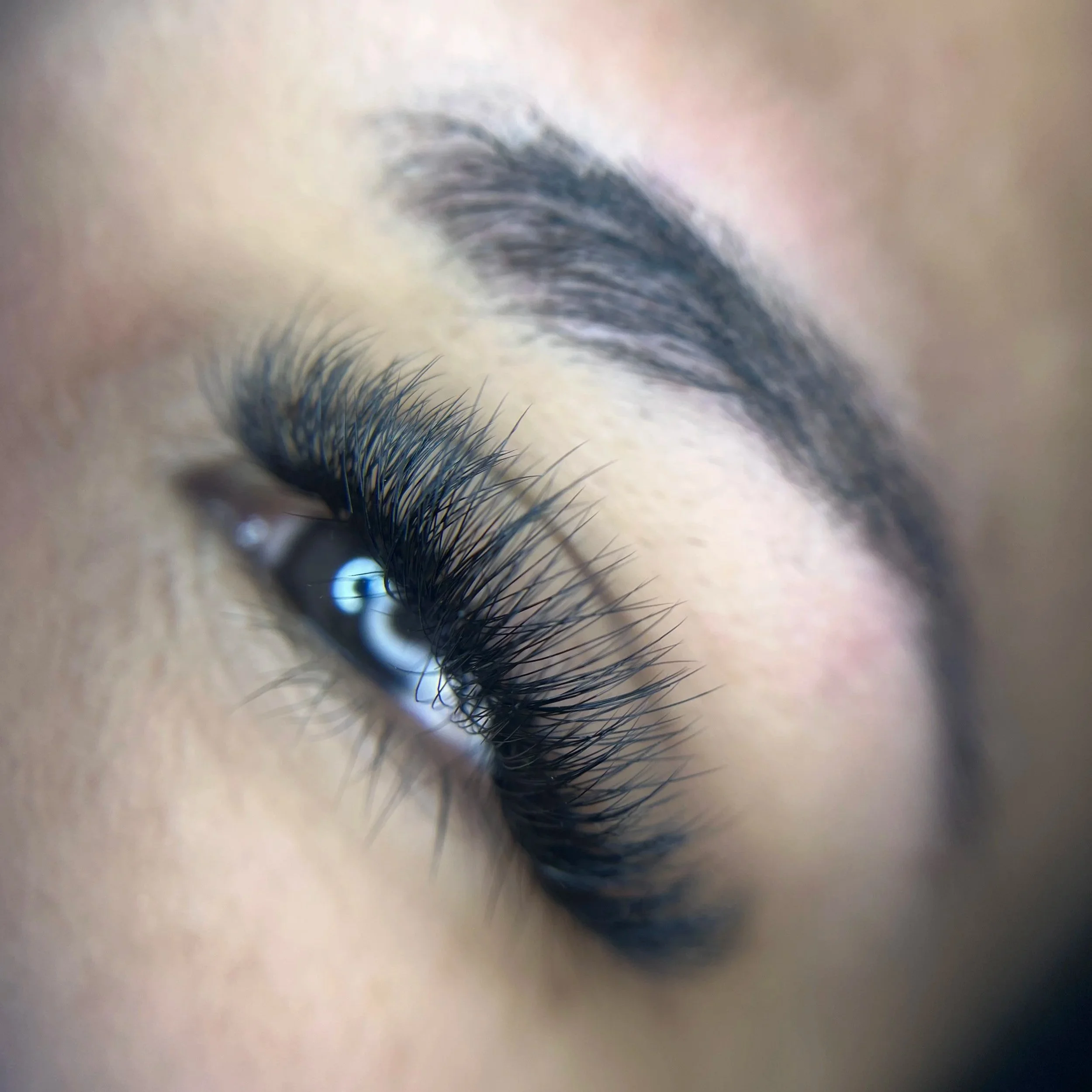 Close-up of a person's eye showing long eyelashes, well-groomed eyebrow, and smooth skin.