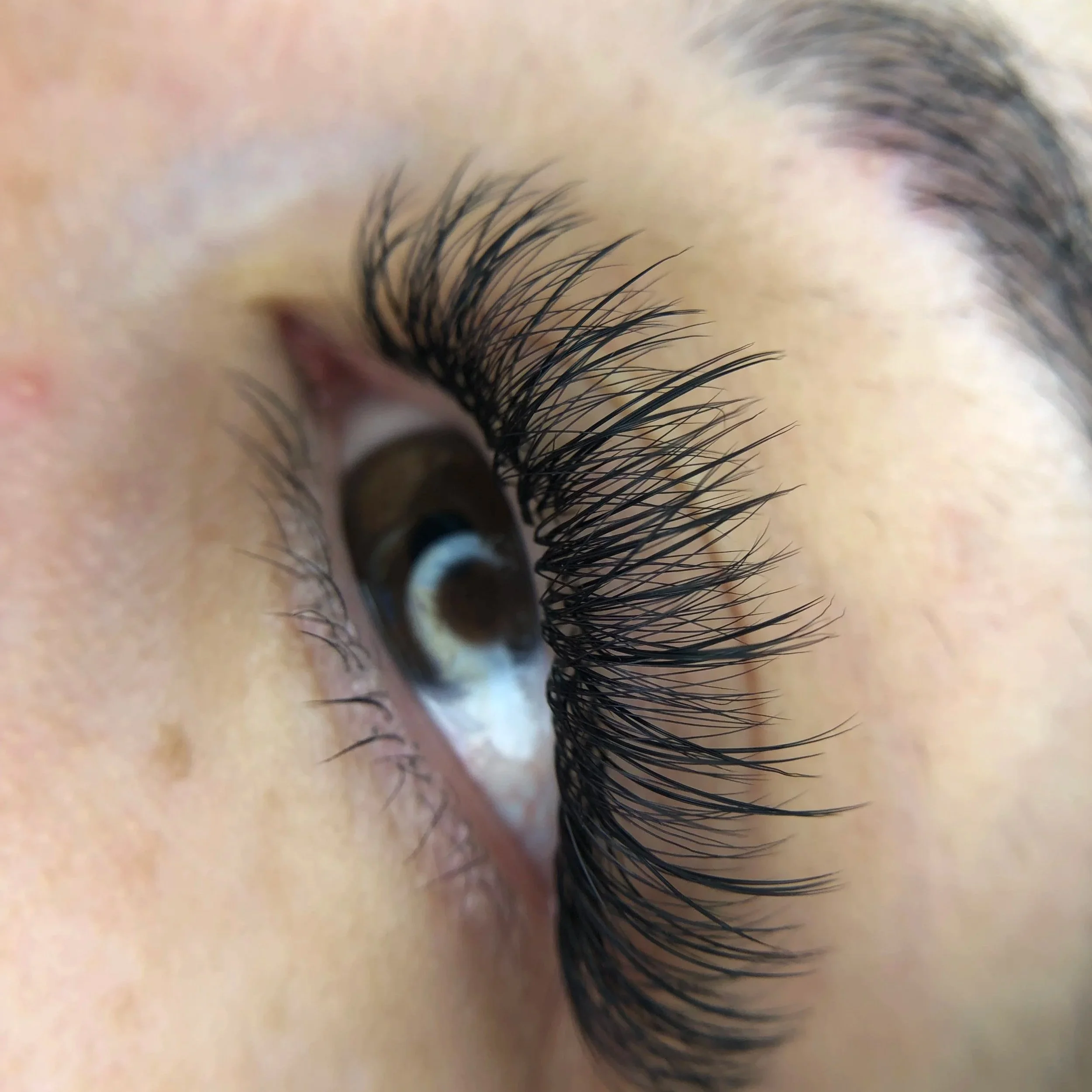 Close-up of a person's eye with long, curled eyelashes and a brown iris.