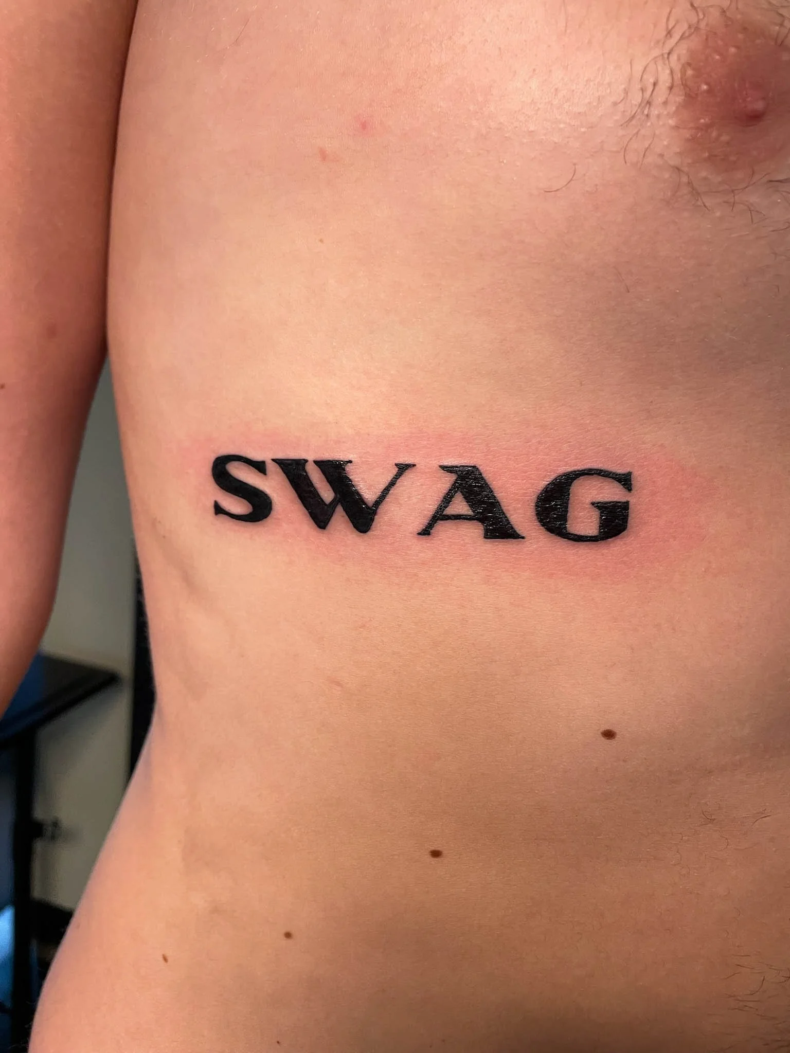 Tattoo with the word 'SWAG' in bold black letters on a person's side ribcage.