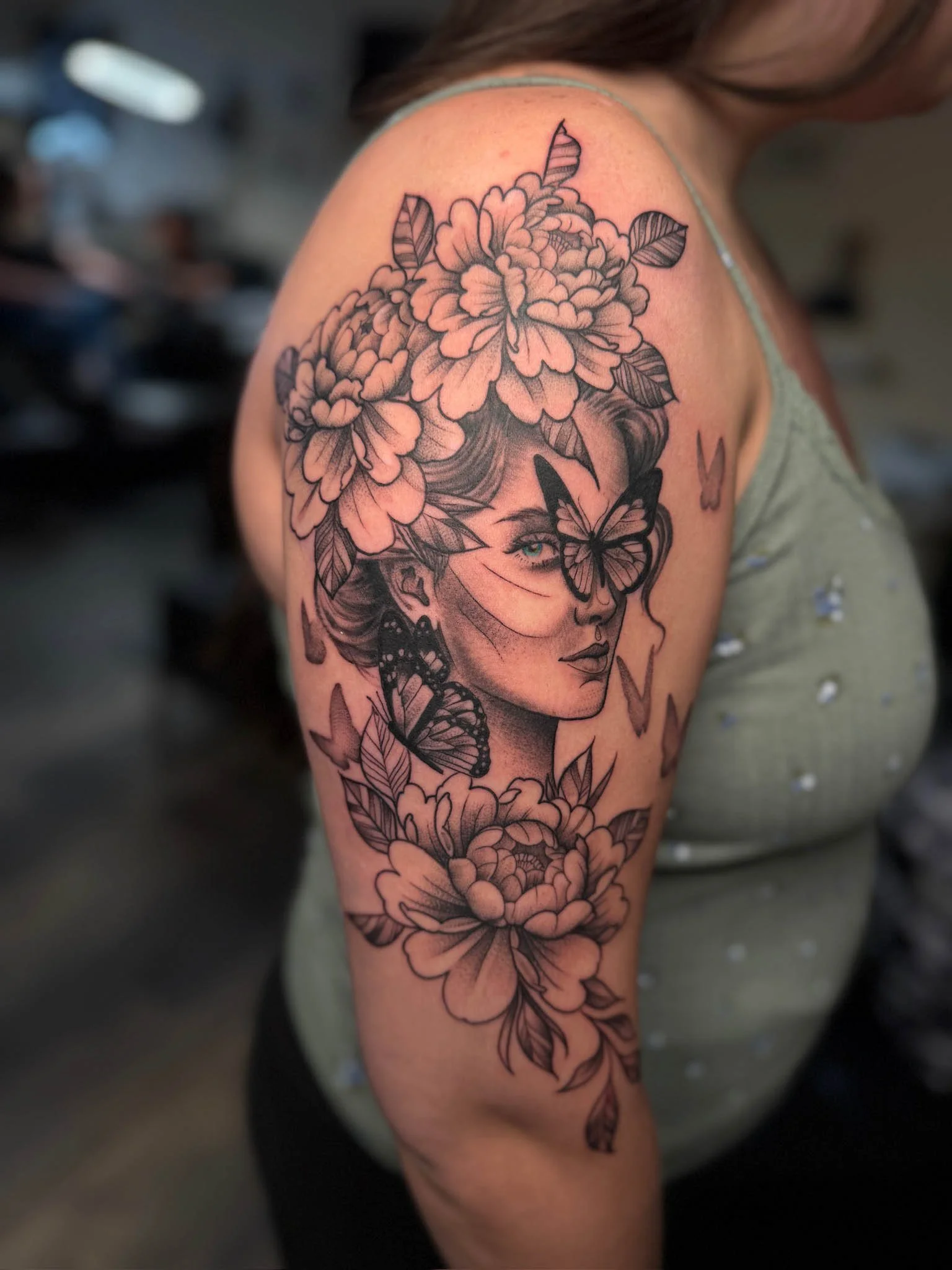 Black and gray tattoo of a woman's face with flowers and butterflies on her shoulder.
