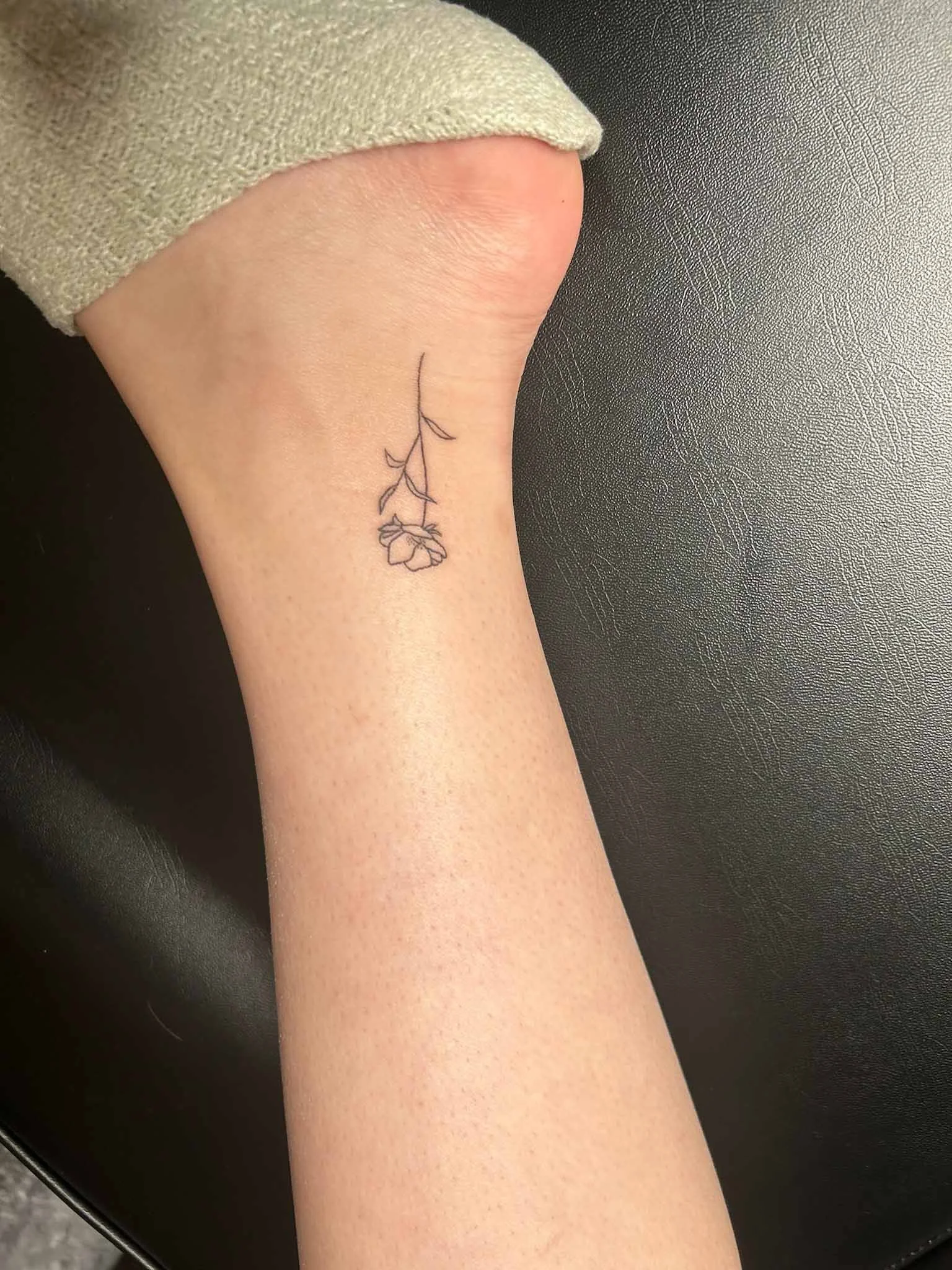 A person's forearm with a minimalistic line tattoo of a flower and a stem.