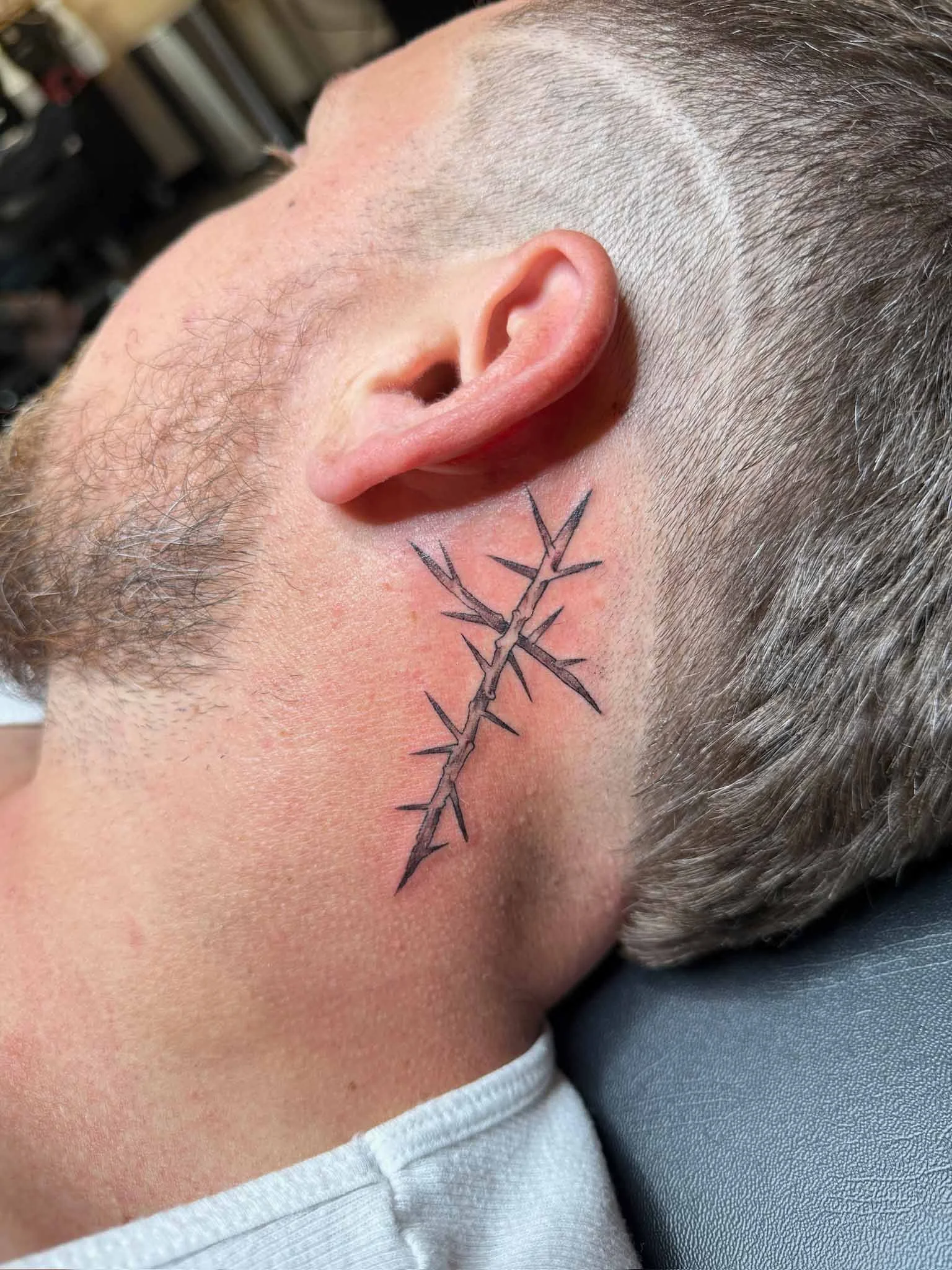 Close-up of a person's neck with a tattoo of a thorny branch extending from behind the ear down the neck.