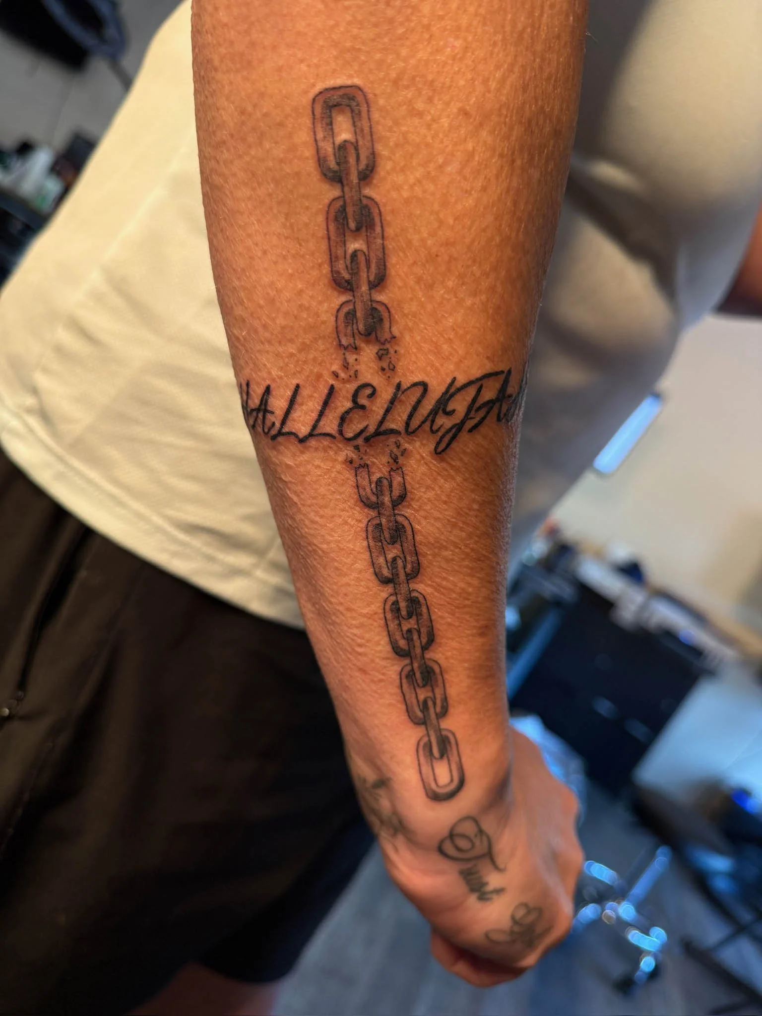 Tattoo of a vertical chain with broken links running down the forearm, intersected by cursive text that reads 'FREEDOM'.