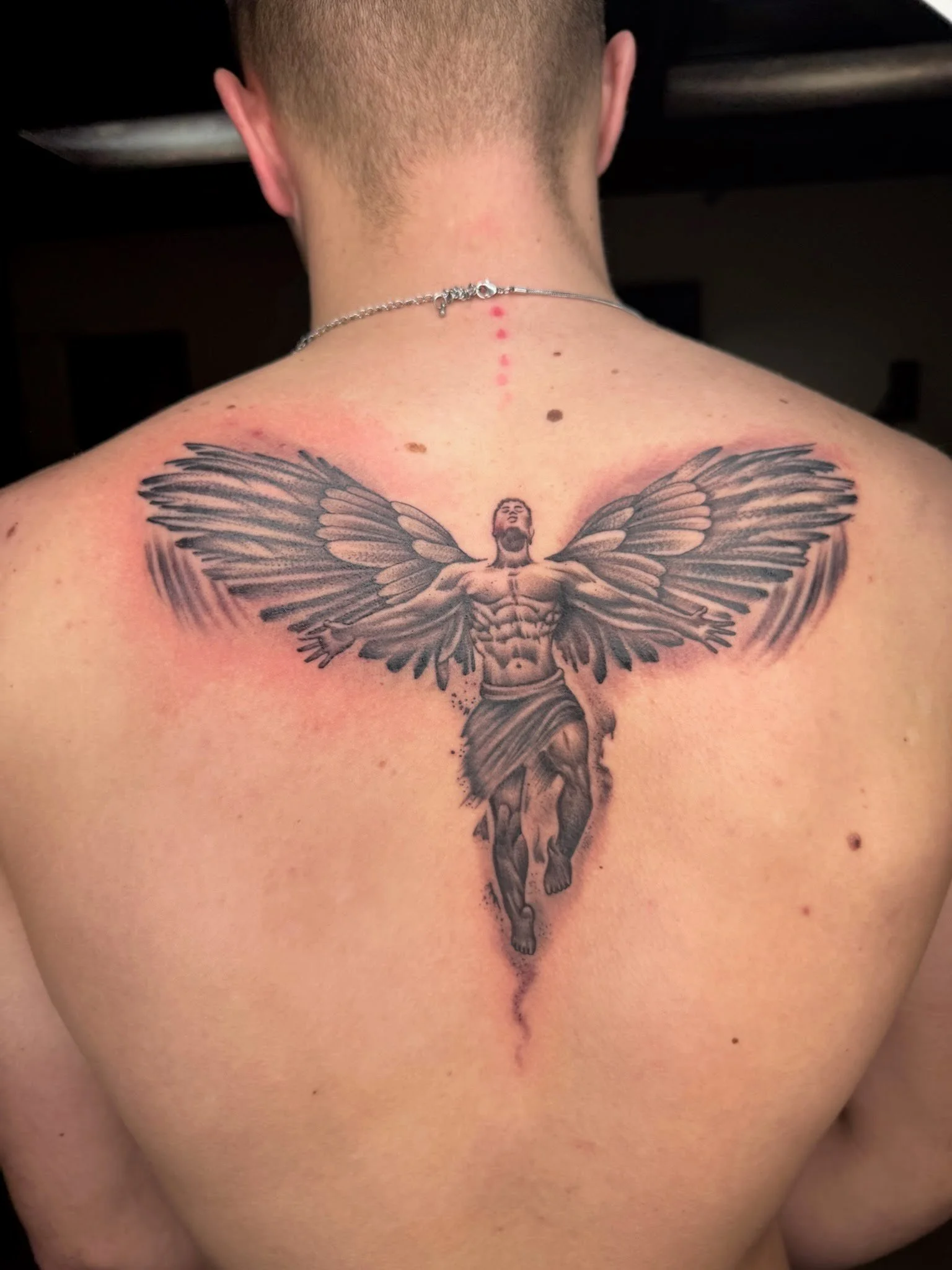 Close up photograph of a black and grey tattoo design of an angel on a man's upper back