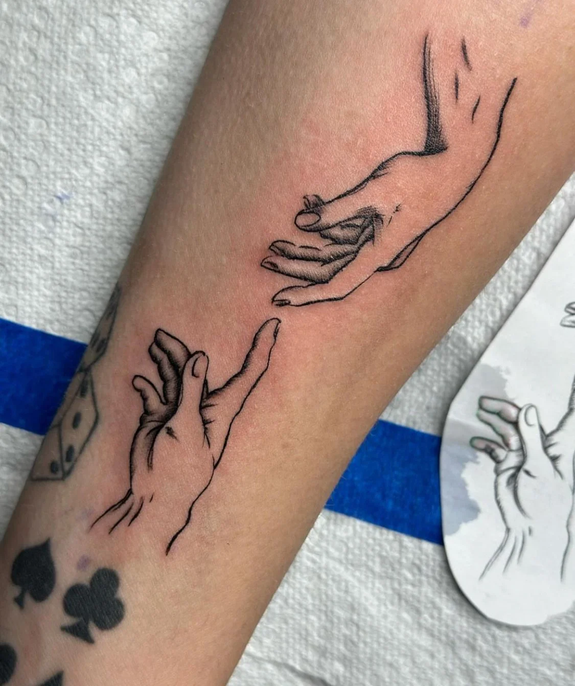 Close-up of photograph of a fine line black and grey tattoo featuring detailed outlines of two hands in a reaching gesture