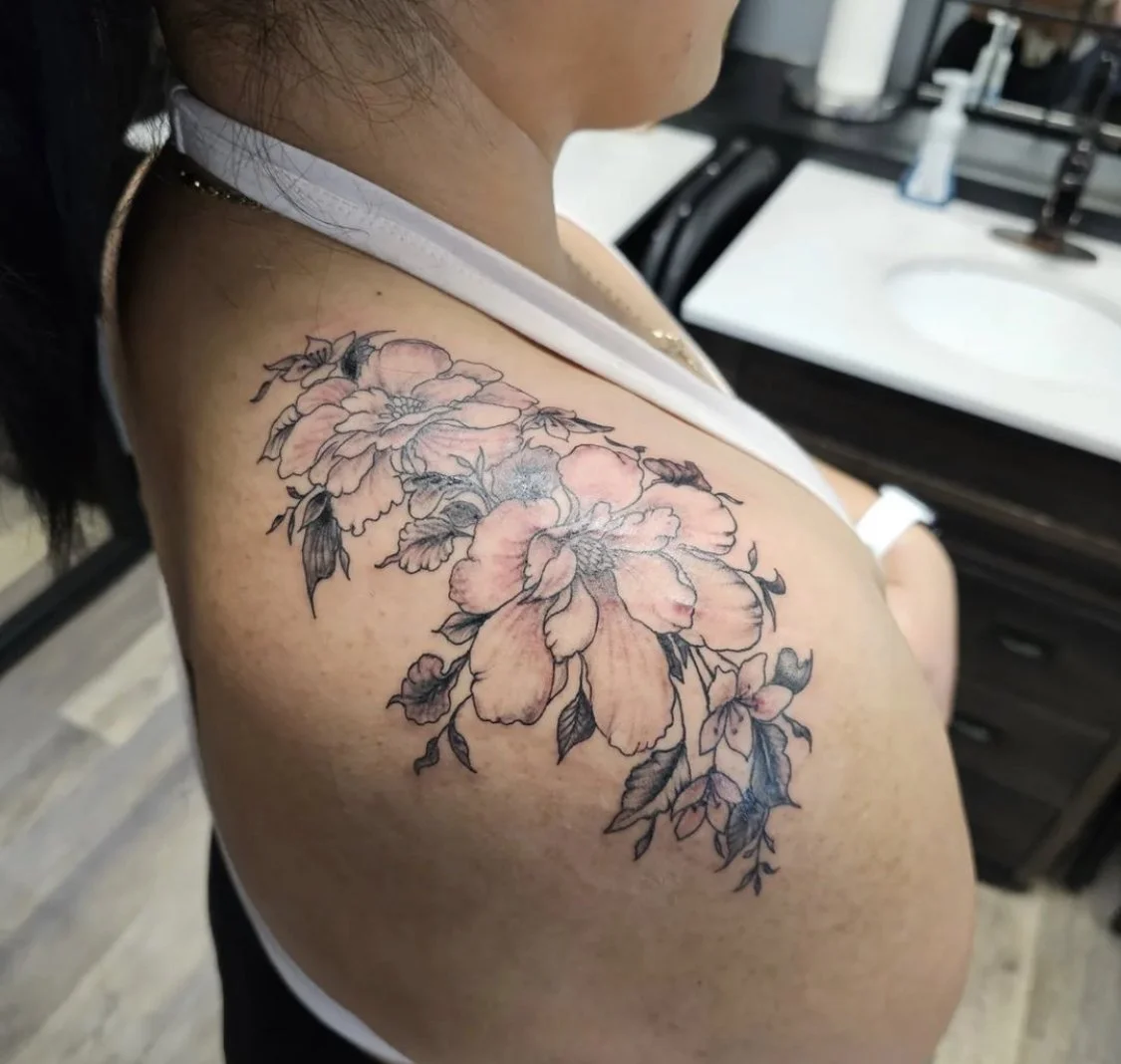 Close-up photograph of a fine line black and grey tattoo of delicate flowers on a woman's shoulder