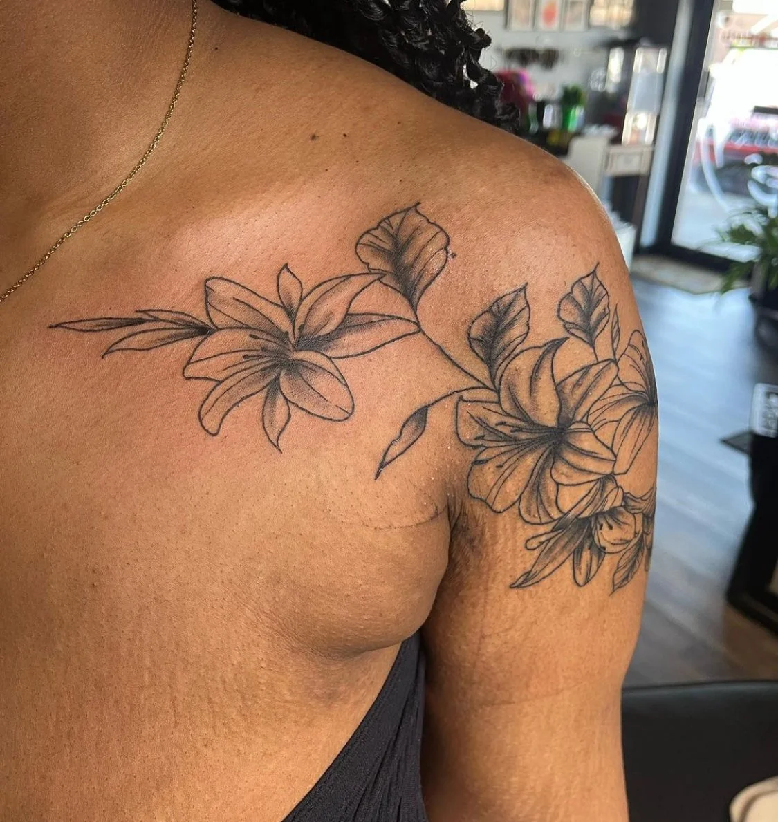 Close-up photograph of a fine line black and grey flower tattoo on shoulder