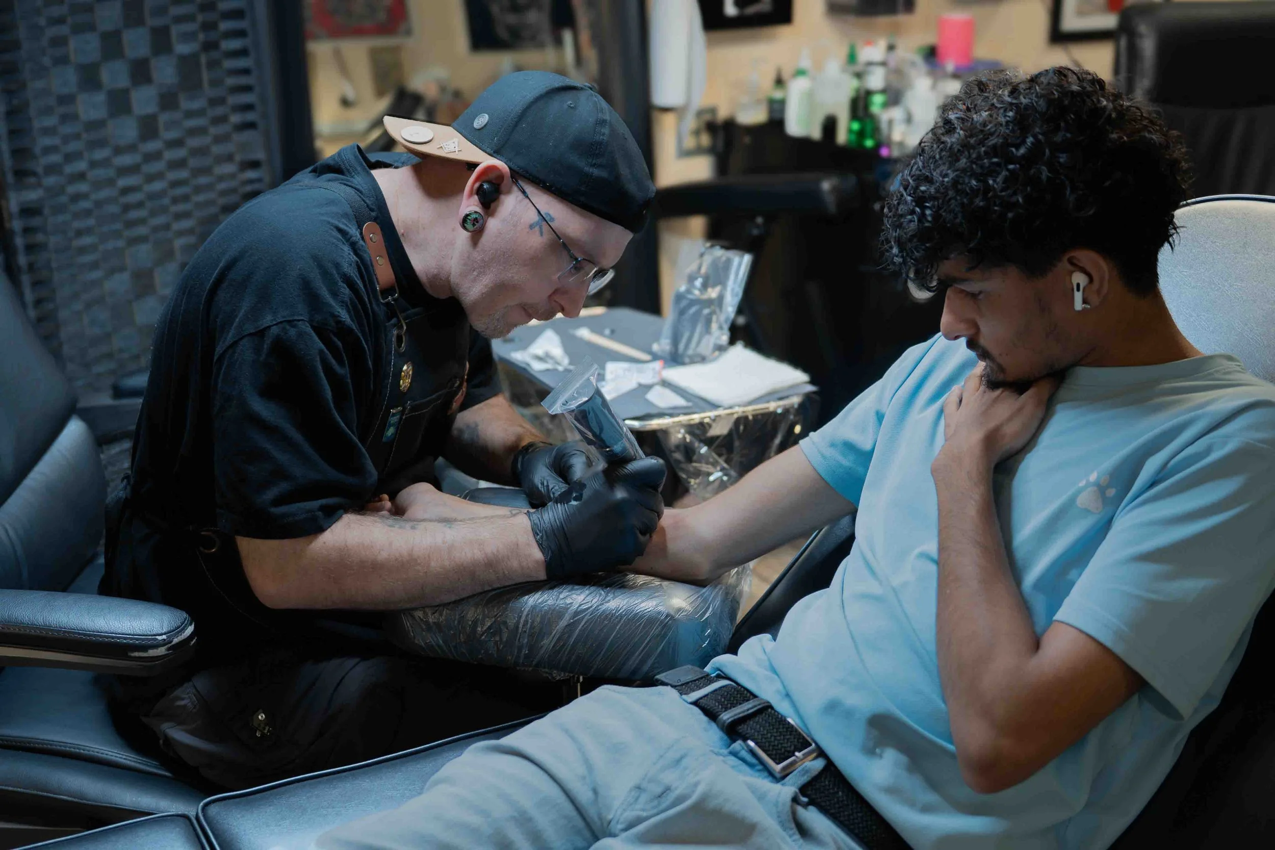 Tattoo artist tattooing a client at a shop workstation.
