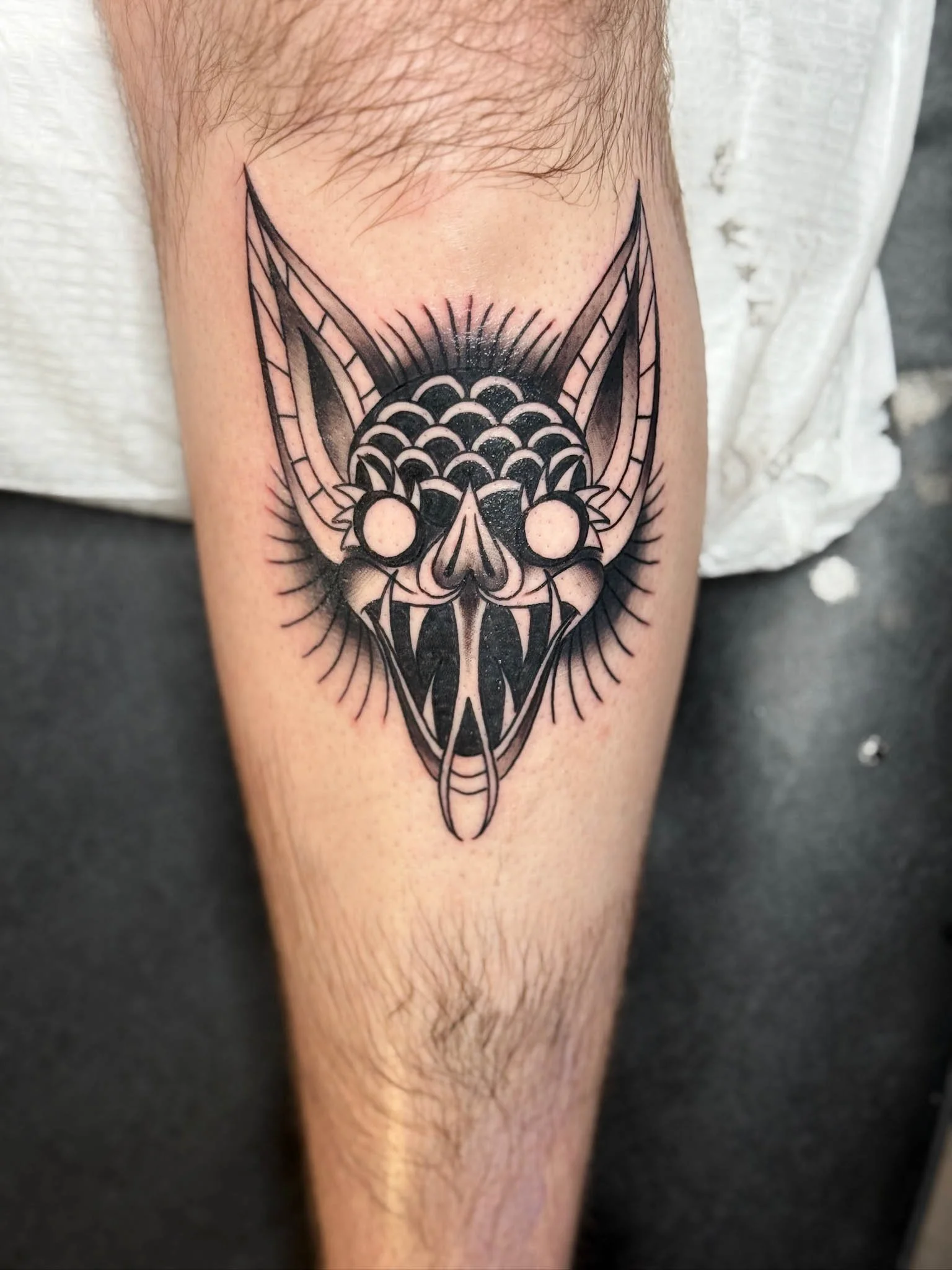 Black and gray tattoo of a stylized bat with exaggerated ears and sharp fangs on a person's thigh.