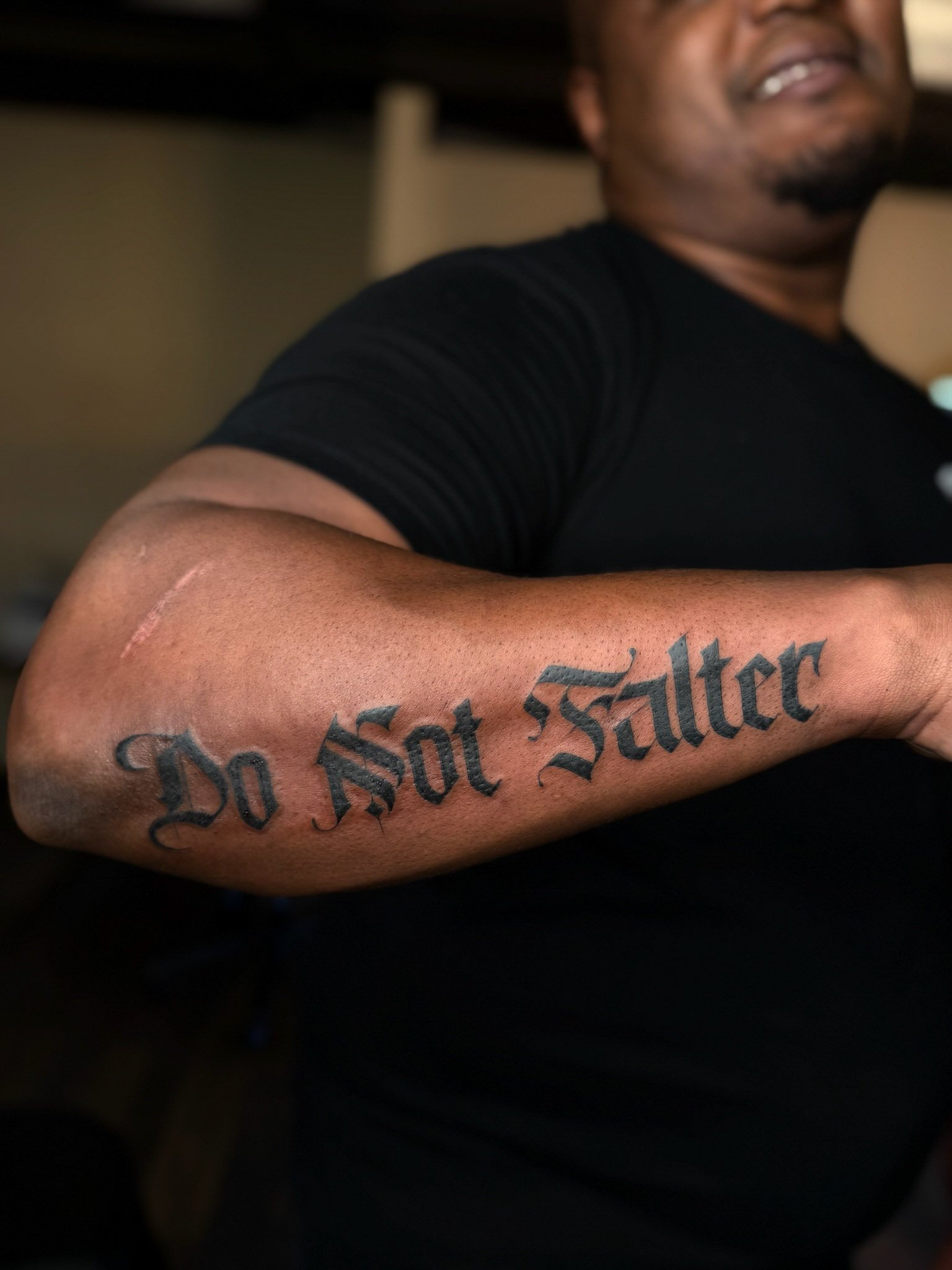 Close-up of a person's arm with a tattoo that says 'Do Not Salter' in black Gothic script.