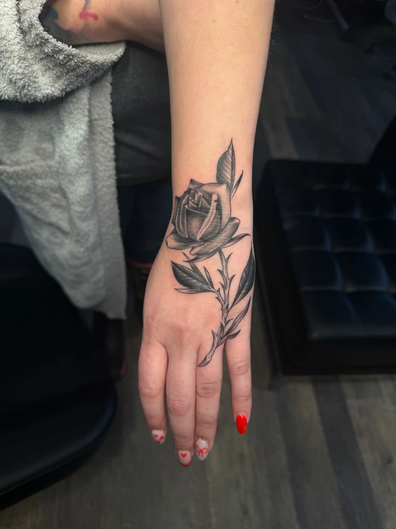 Black and gray tattoo of a rose with leaves on a person's wrist and hand.