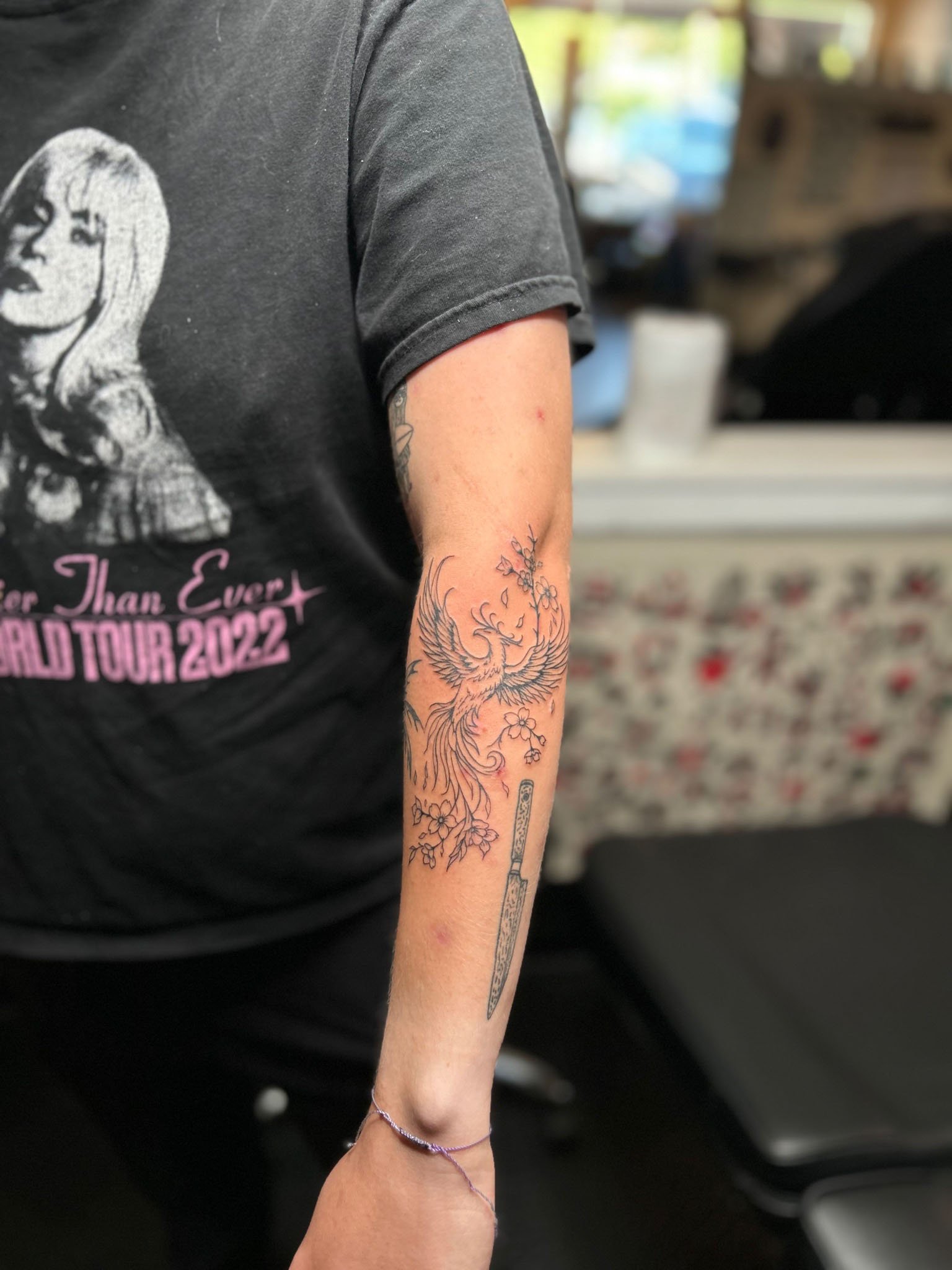 Detailed bird forearm tattoo on a person wearing a dark graphic t-shirt