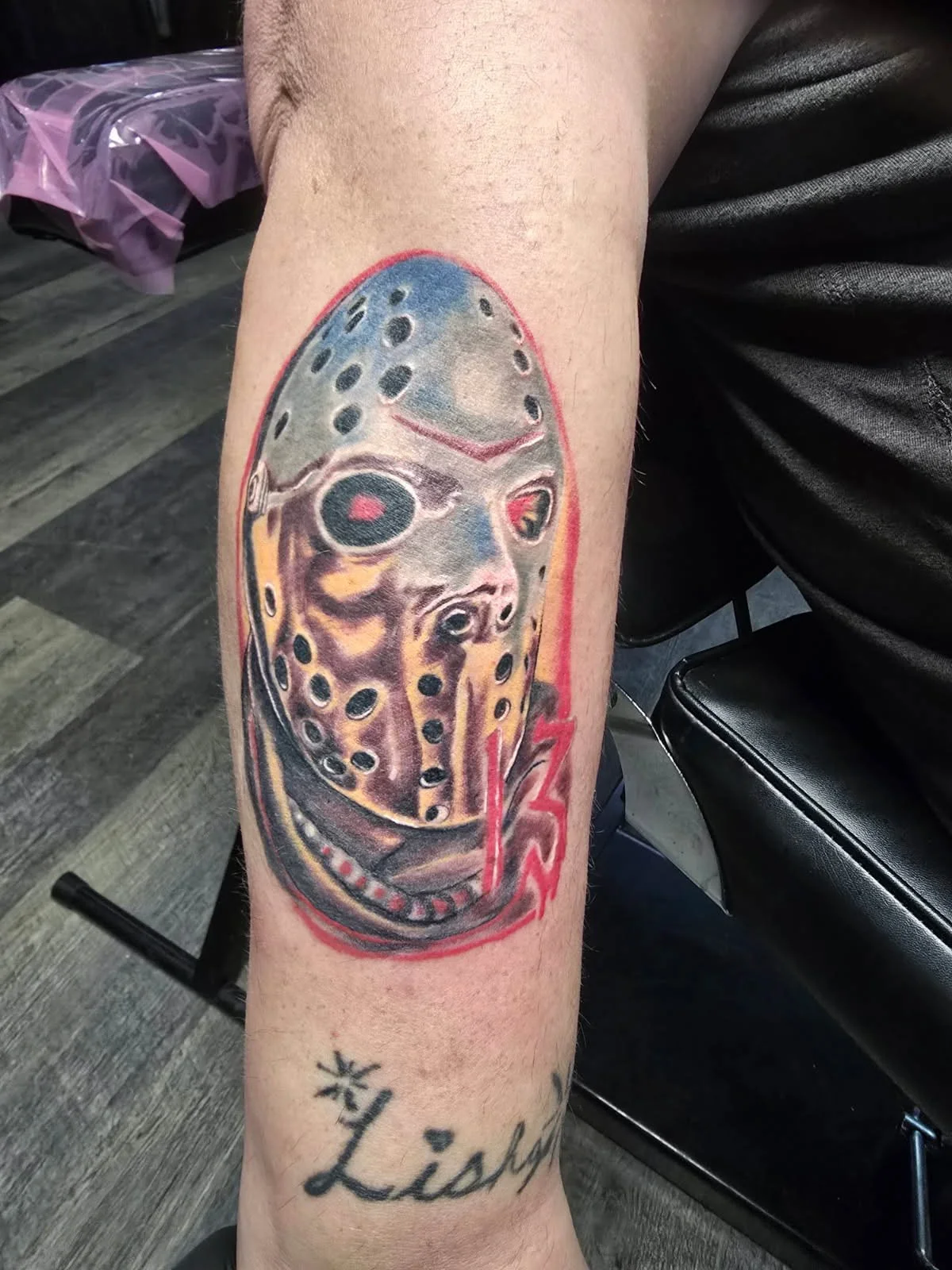Tattoo of a hockey mask from Friday the 13th, with red accents and the word "Lishy" written below.