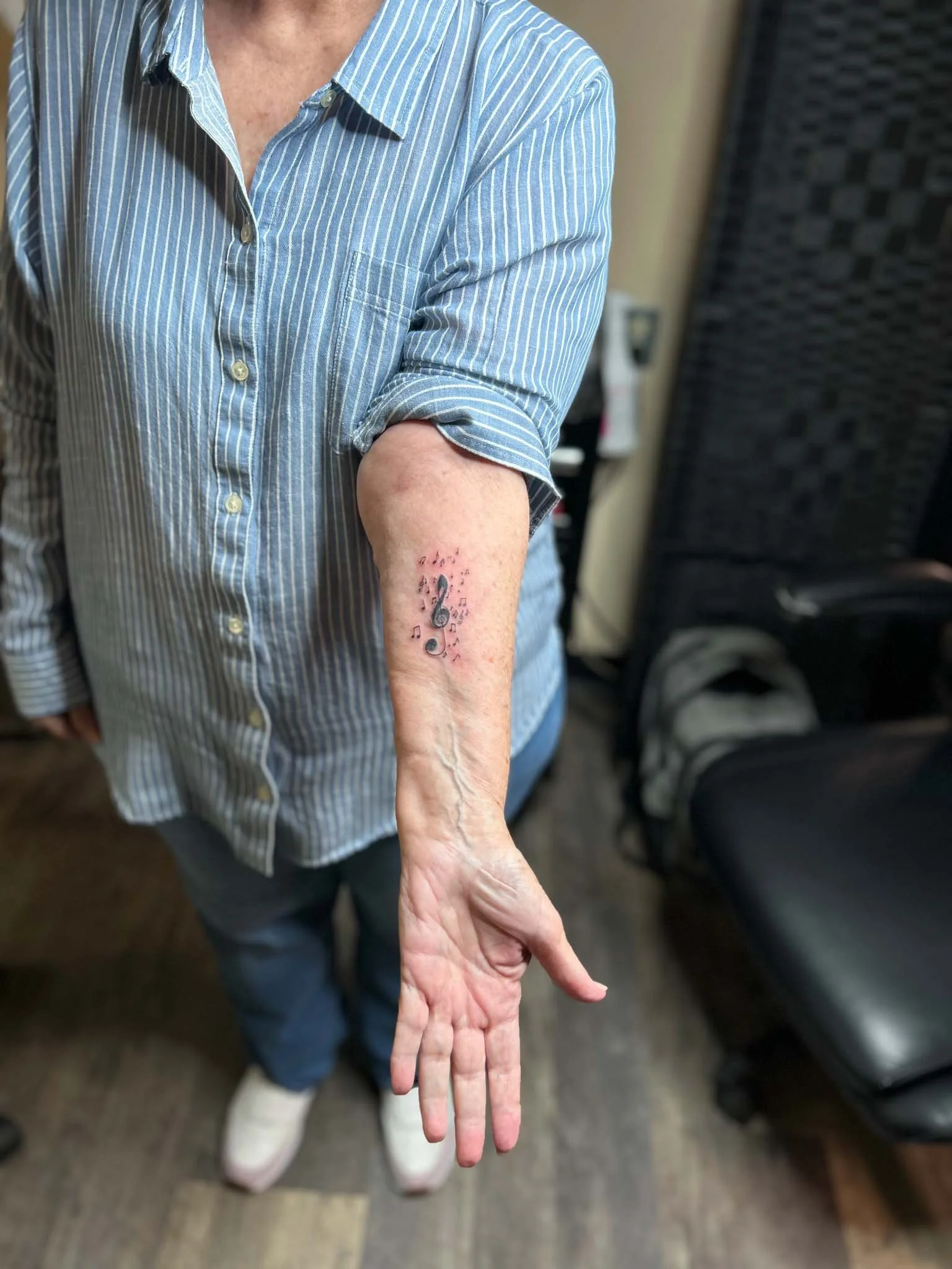 Person in a light blue button-down shirt displaying a musical note in forearm tattoo