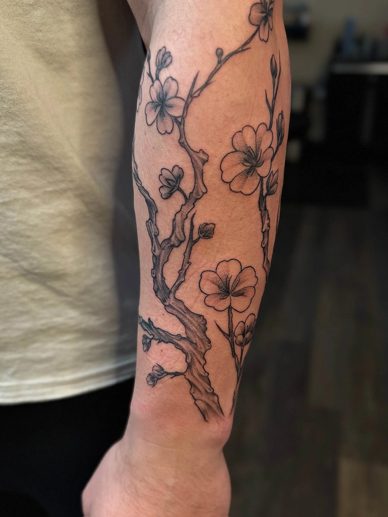 Black outline tattoo of a flowering branch on a person's arm with blossoms and buds.