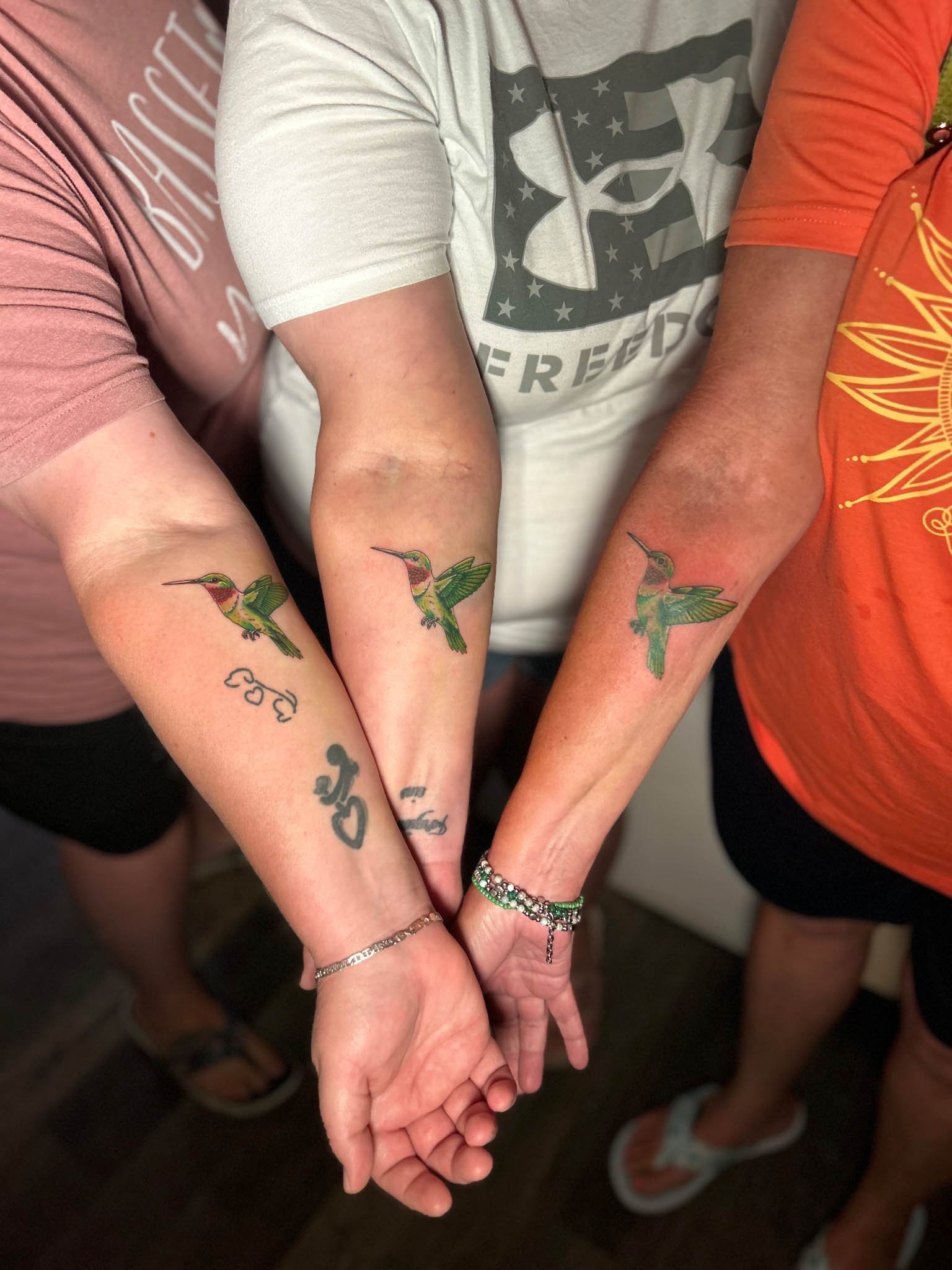 Forearms side-by-side displaying matching humming bird tattoos